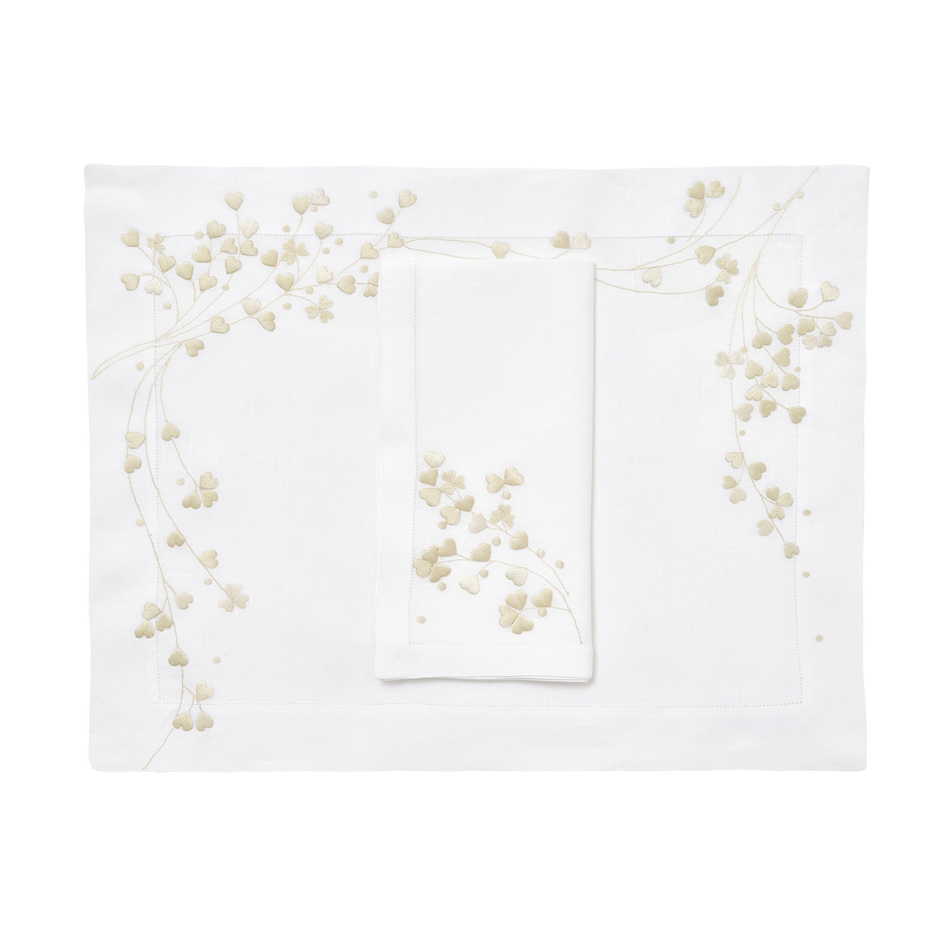 Ivory embroidered hearts, Anagramme Embroidery, shown on placemat with a folded napkin, finished with a hemstitch on white linen, on a white background.
