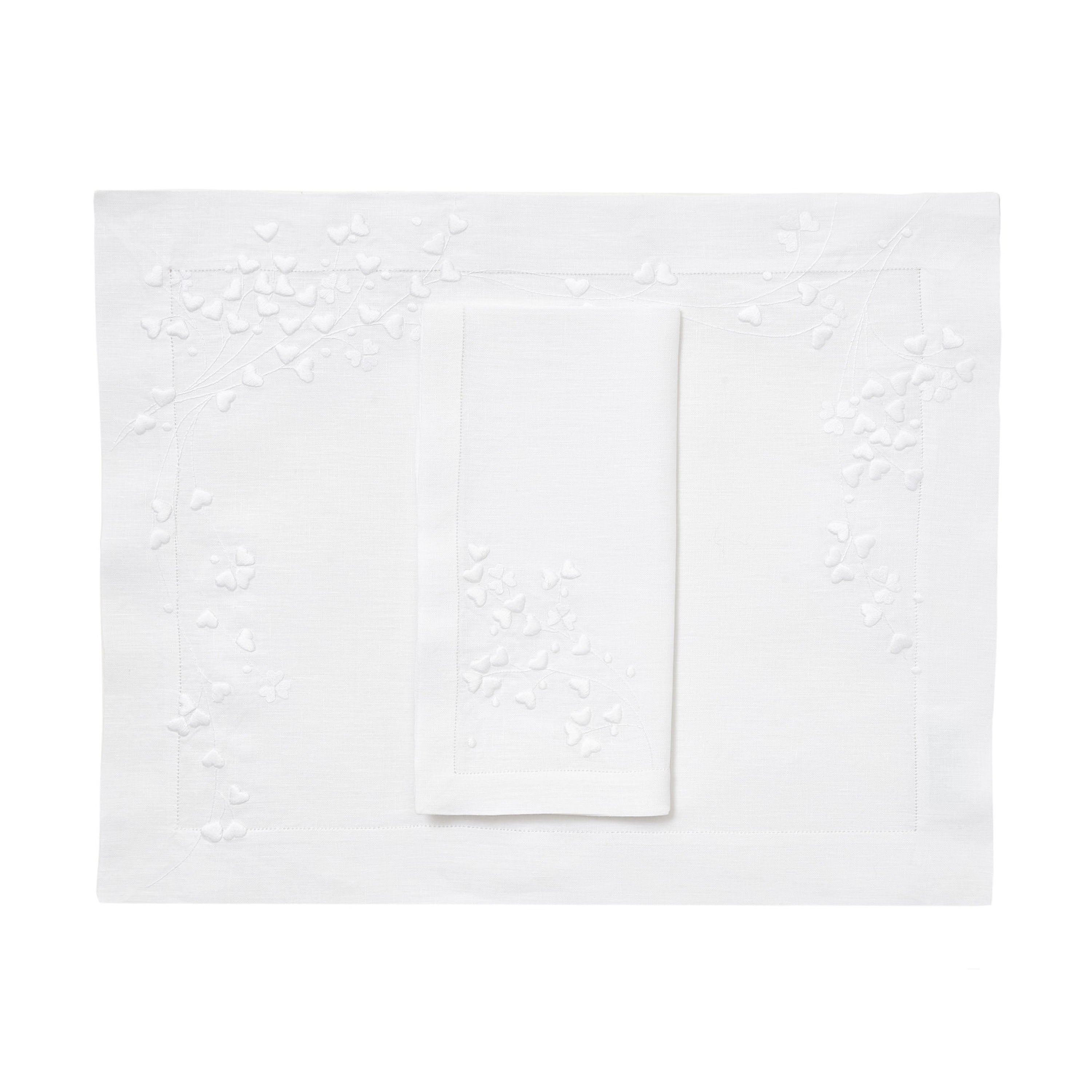 White embroidered hearts, Anagramme Embroidery, shown on placemat with a folded napkin, finished with a hemstitch on white linen, on a white background.