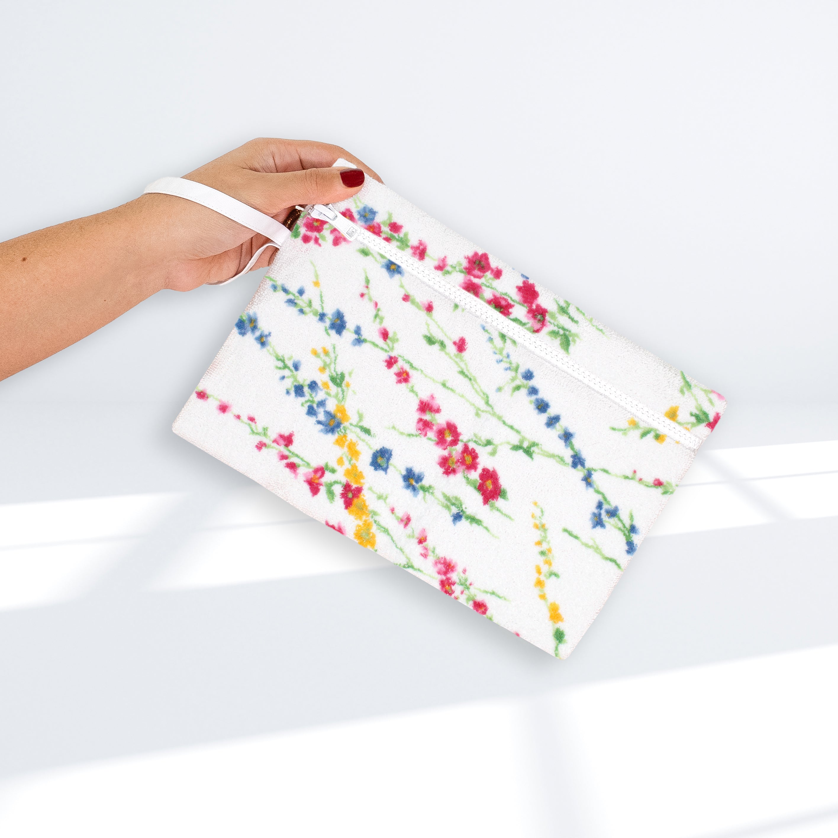 Multicolored floral-patterned pouch, white zipper, and white wrist band, on a white background