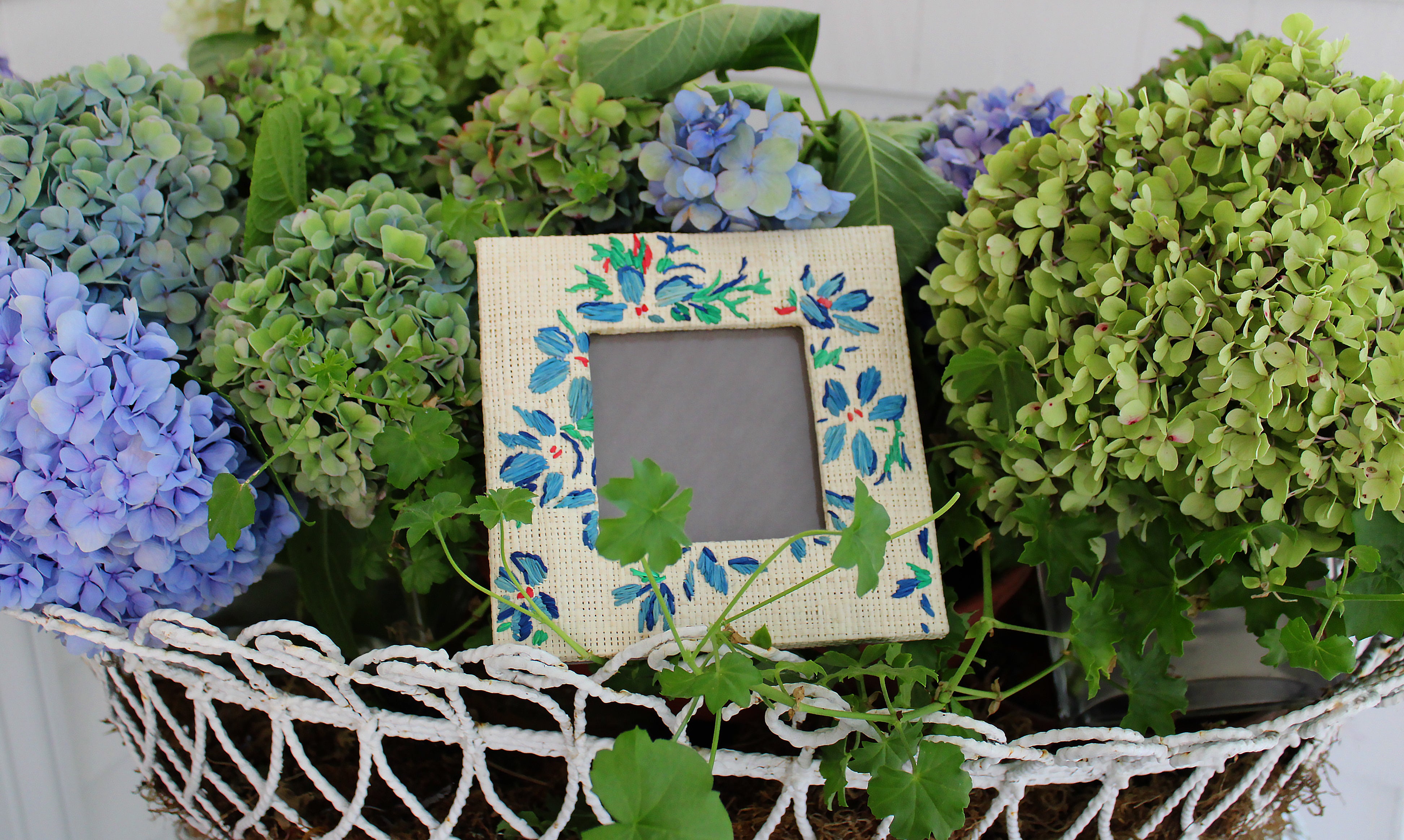 Decorative picture frame with floral design surrounded by green and blue hydrangeas.