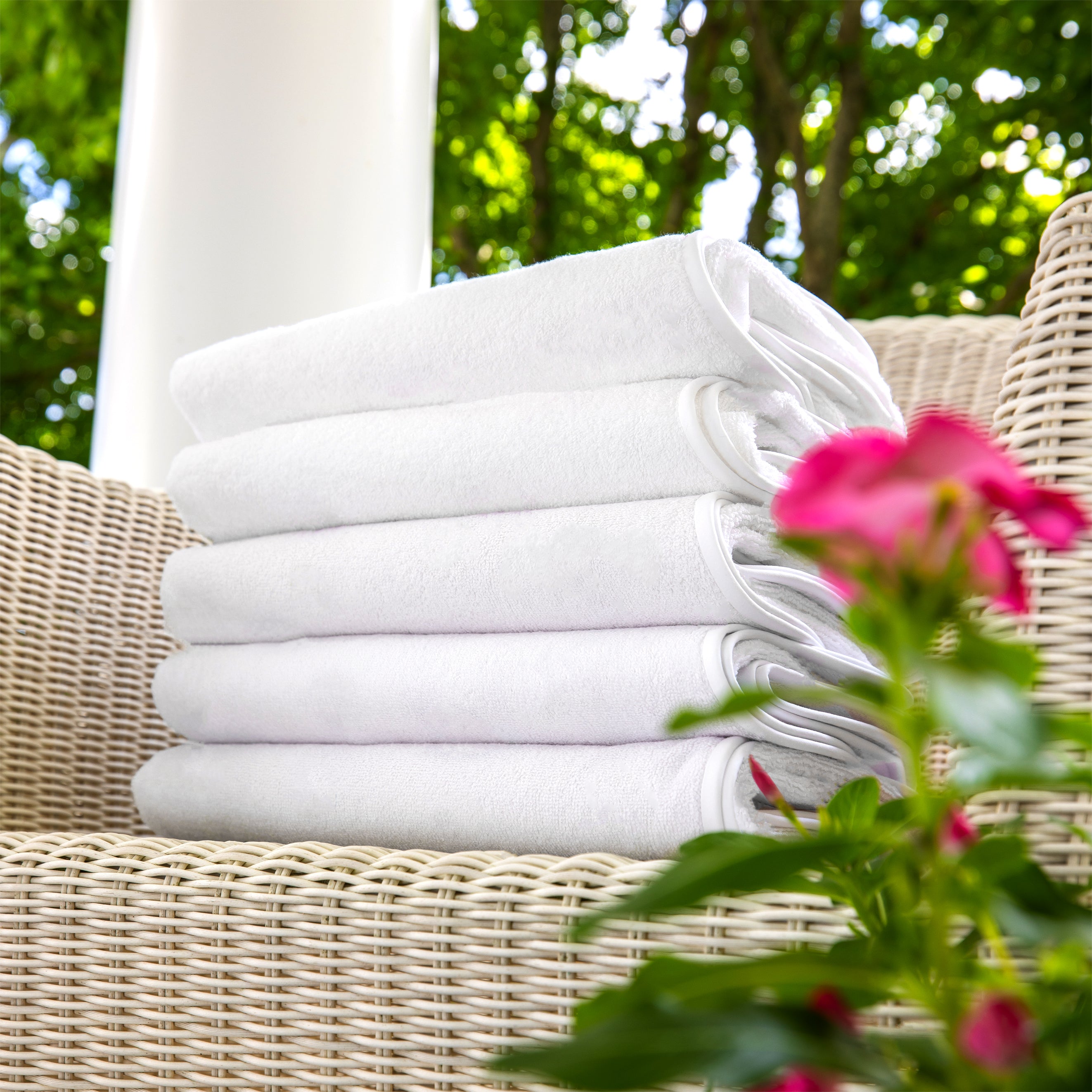 Stack of white towels on a wicker chair with greenery and flowers in the background