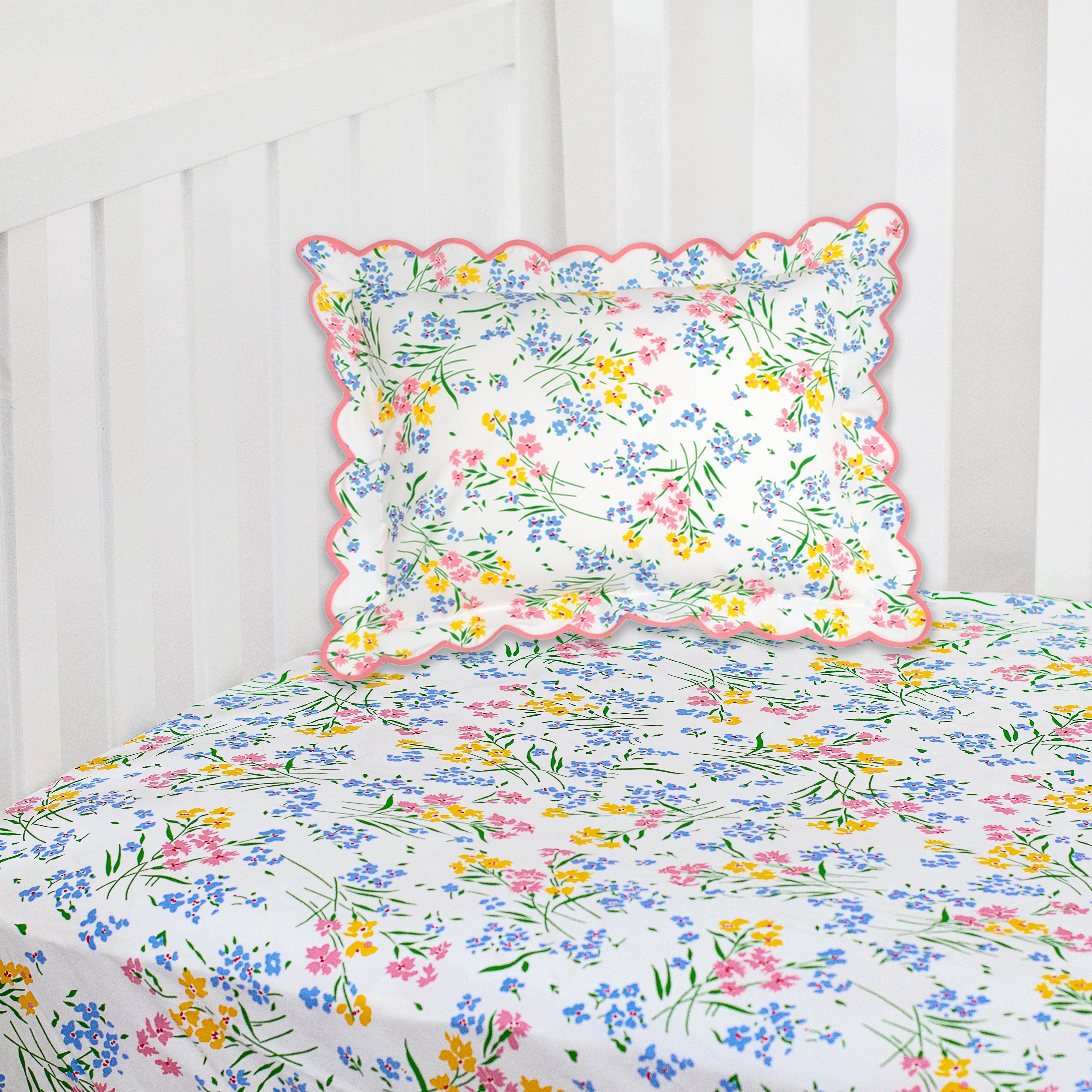 Printed multi color print (Fleurs des Champs in Pink, Blue, Yellow and Green) on crib fitted sheet, corner shot of crib with scallop pink boudoir in matching print.