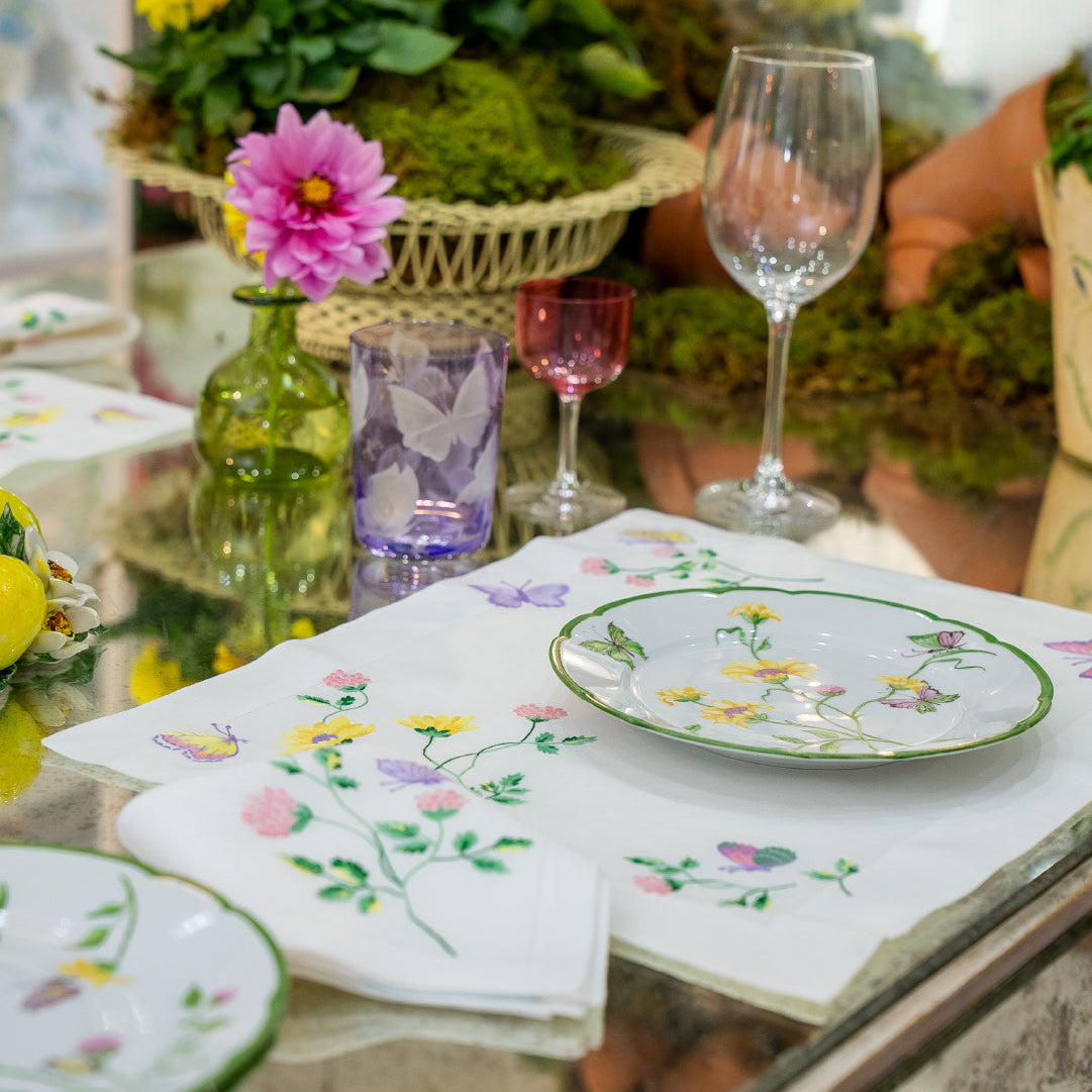 Embroidered florals and butterflies (in pink, yellow, lilac and green) Table linens displayed on glass table, with fresh flowers, and assorted colored glass stemware.