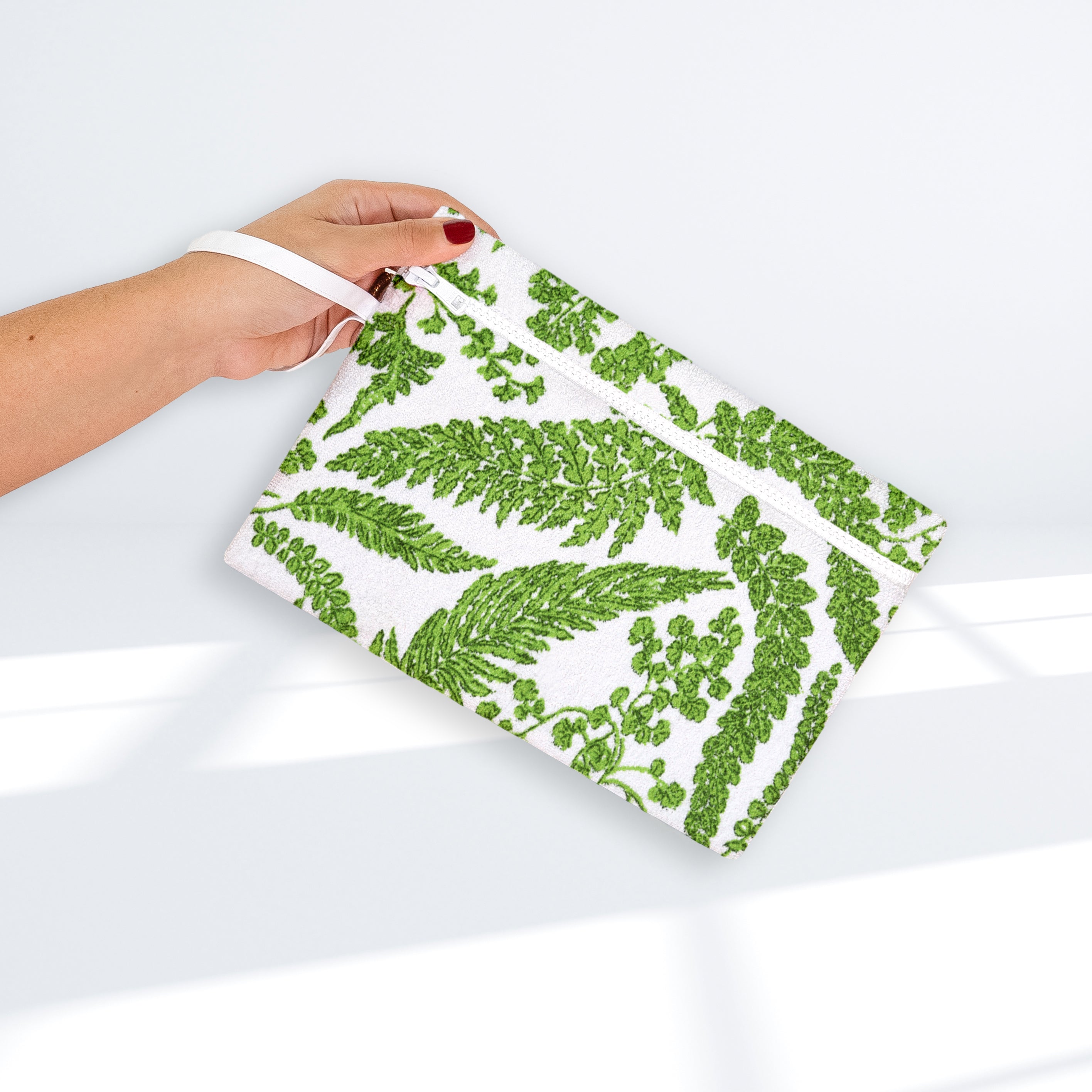 Green floral-patterned pouch, white zipper, and white wrist band, on a white background
