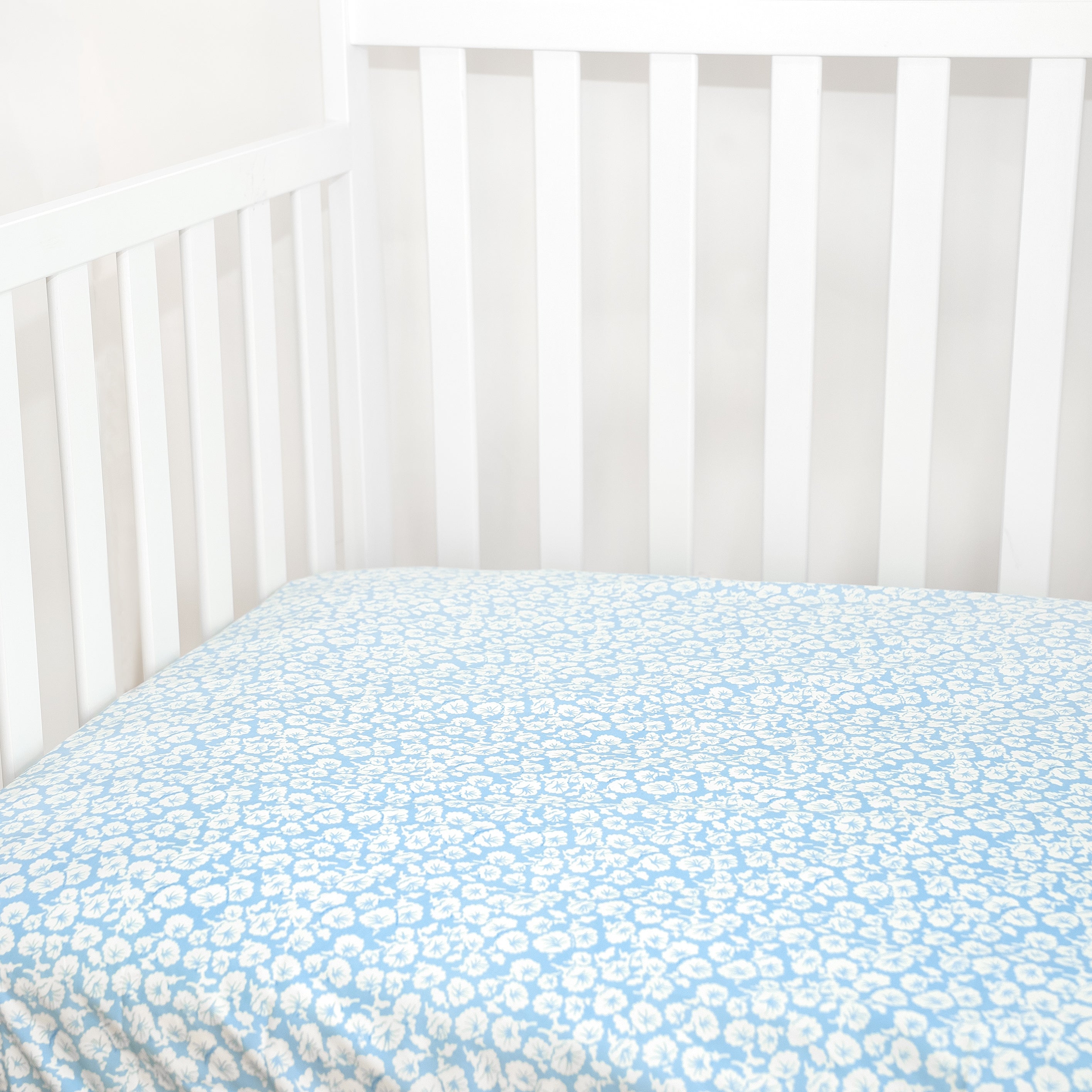 white floral pattern on baby blue background fitted sheet in crib