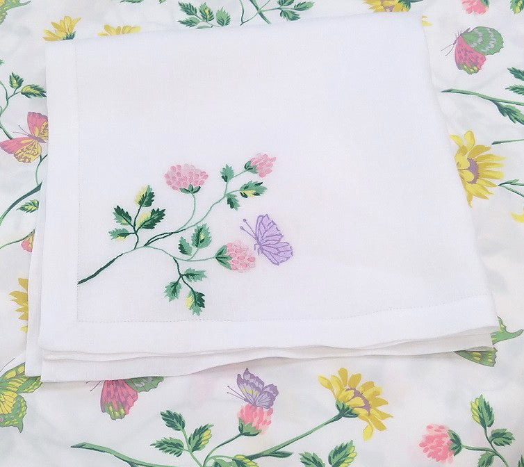 Printed and embroidered florals and butterflies (in pink, yellow, lilac and green) 20x20" napkin displayed on fabric.