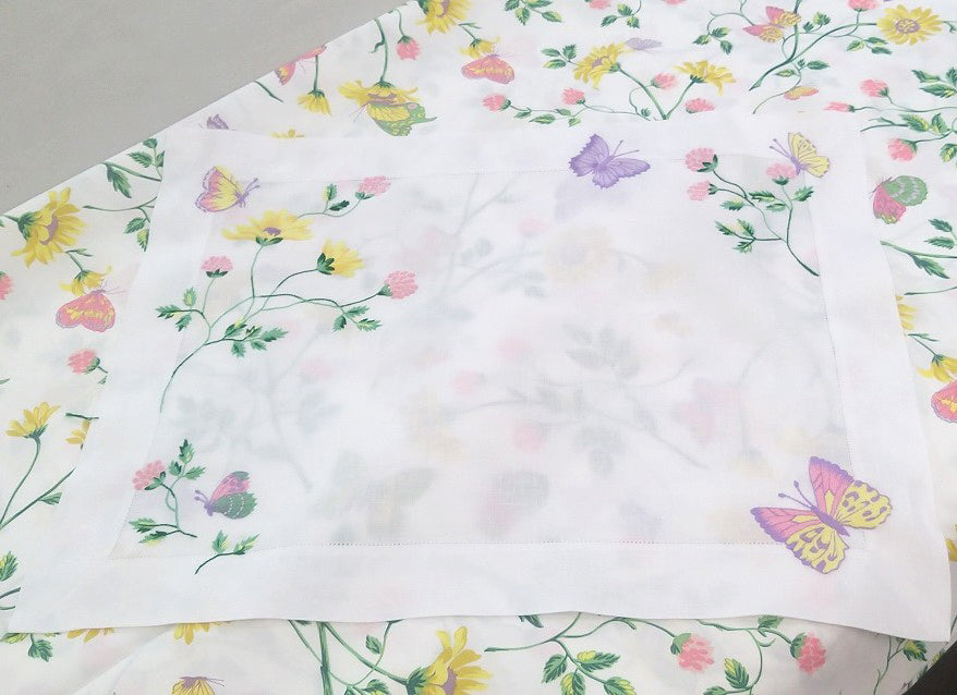 Printed and embroidered florals and butterflies (in pink, yellow, lilac and green) placemat displayed on fabric.