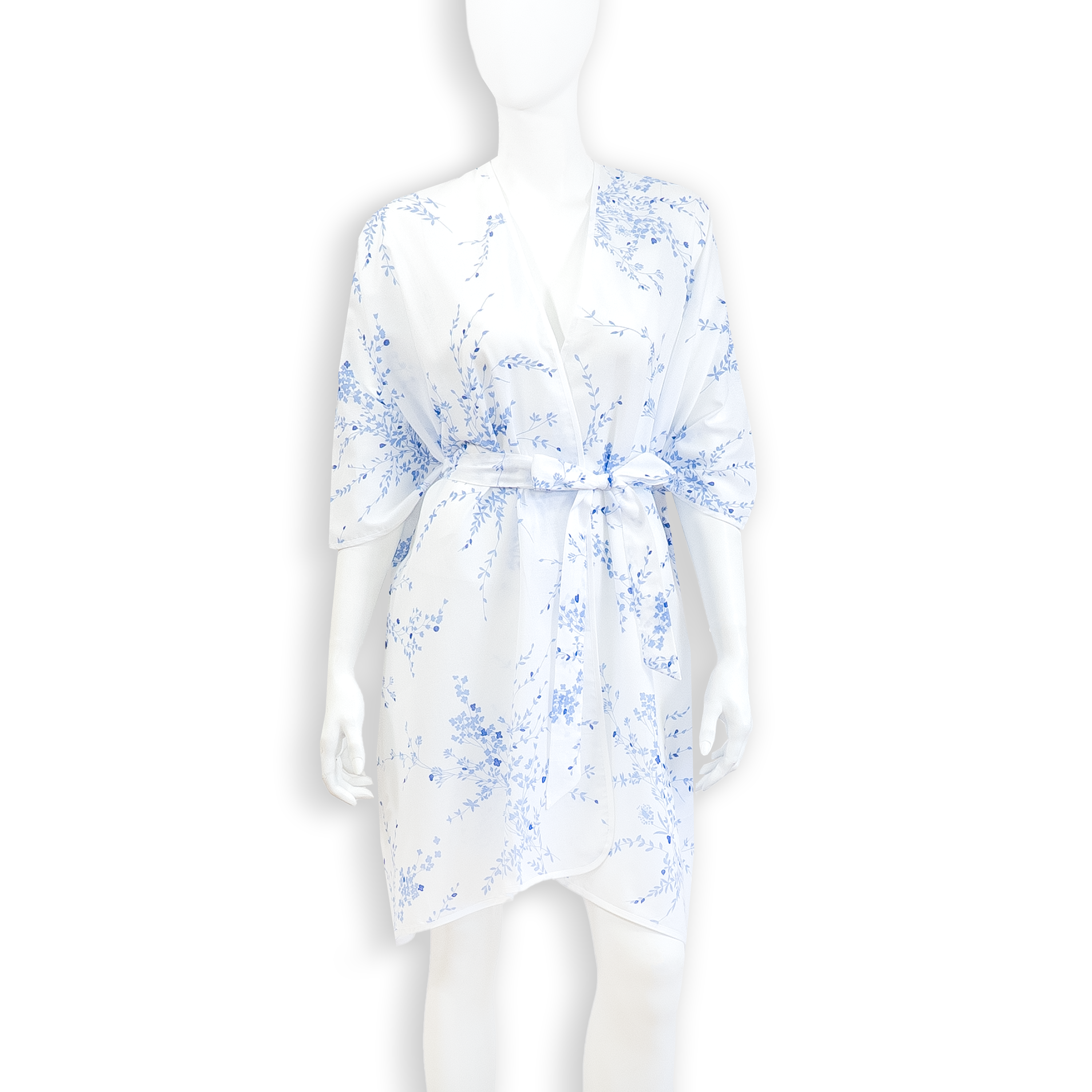 Solid White voile fabric kaftan with jete de fleurs blue floral print, white bias finish. With a matching belt tied with a bow around the hip, on a mannequin with a white background.