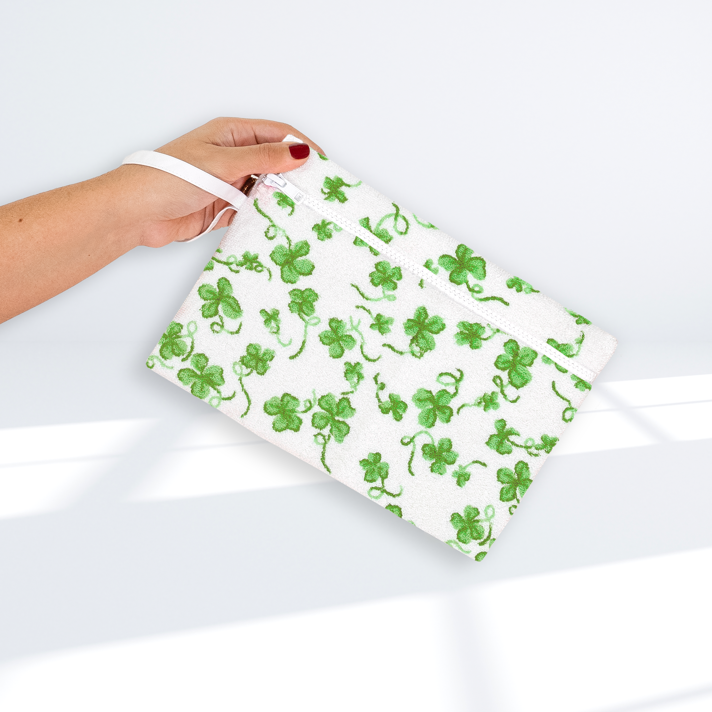 Green clover-patterned pouch, white zipper, and white wrist band, on a white background
