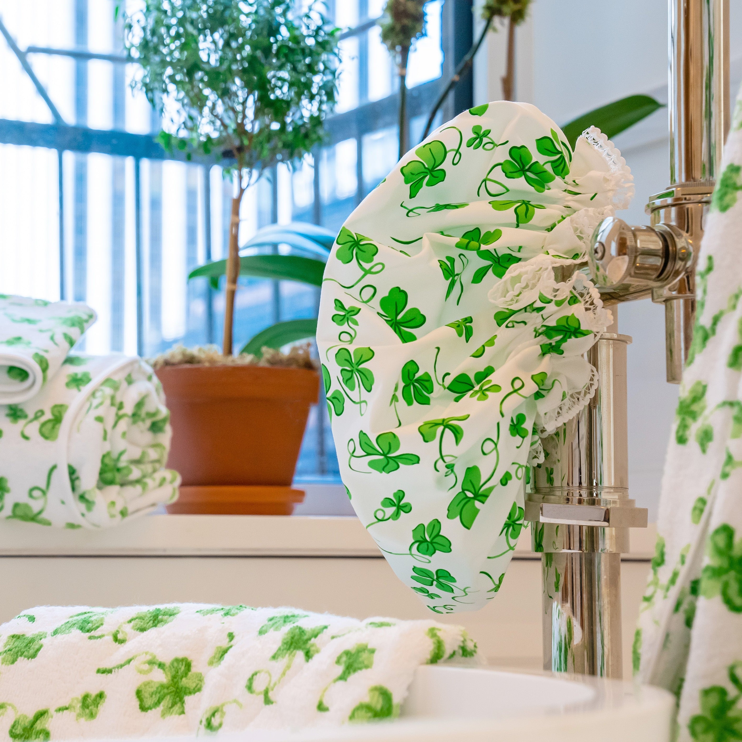 Bathroom scene with our Trefles green patterned shower cap and towels. Potted plant by the window adds freshness. Warm, inviting atmosphere.
