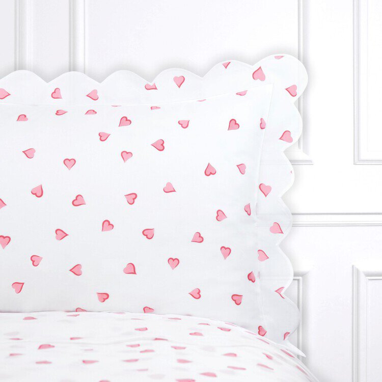 A close-up of a white pillow sham with a scalloped edge and a pink heart pattern.