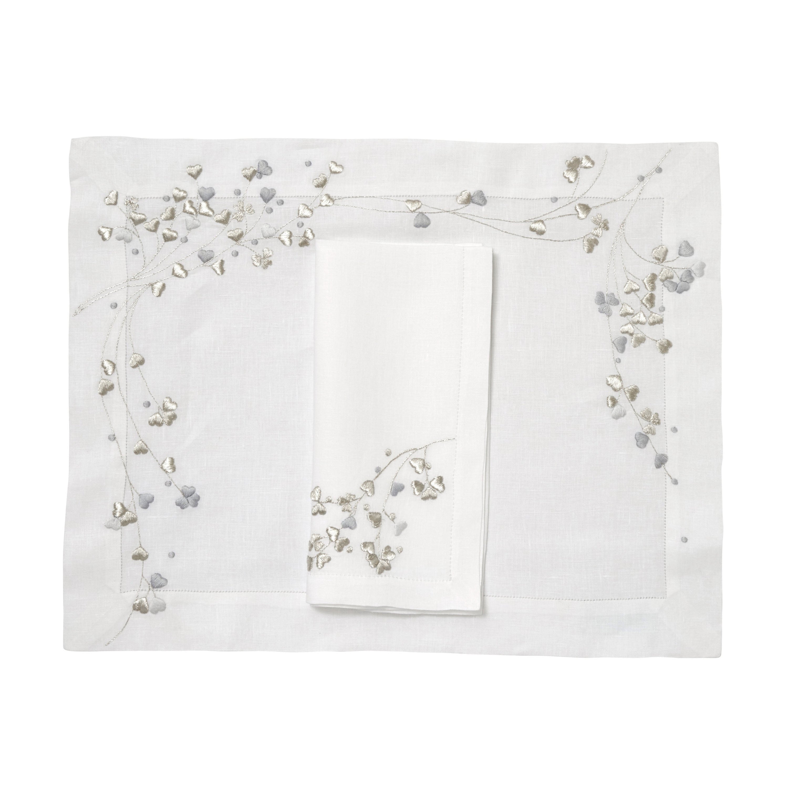 Silver and grey embroidered hearts, Anagramme Embroidery, shown on placemat with a folded napkin, finished with a hemstitch on white linen, on a white background.