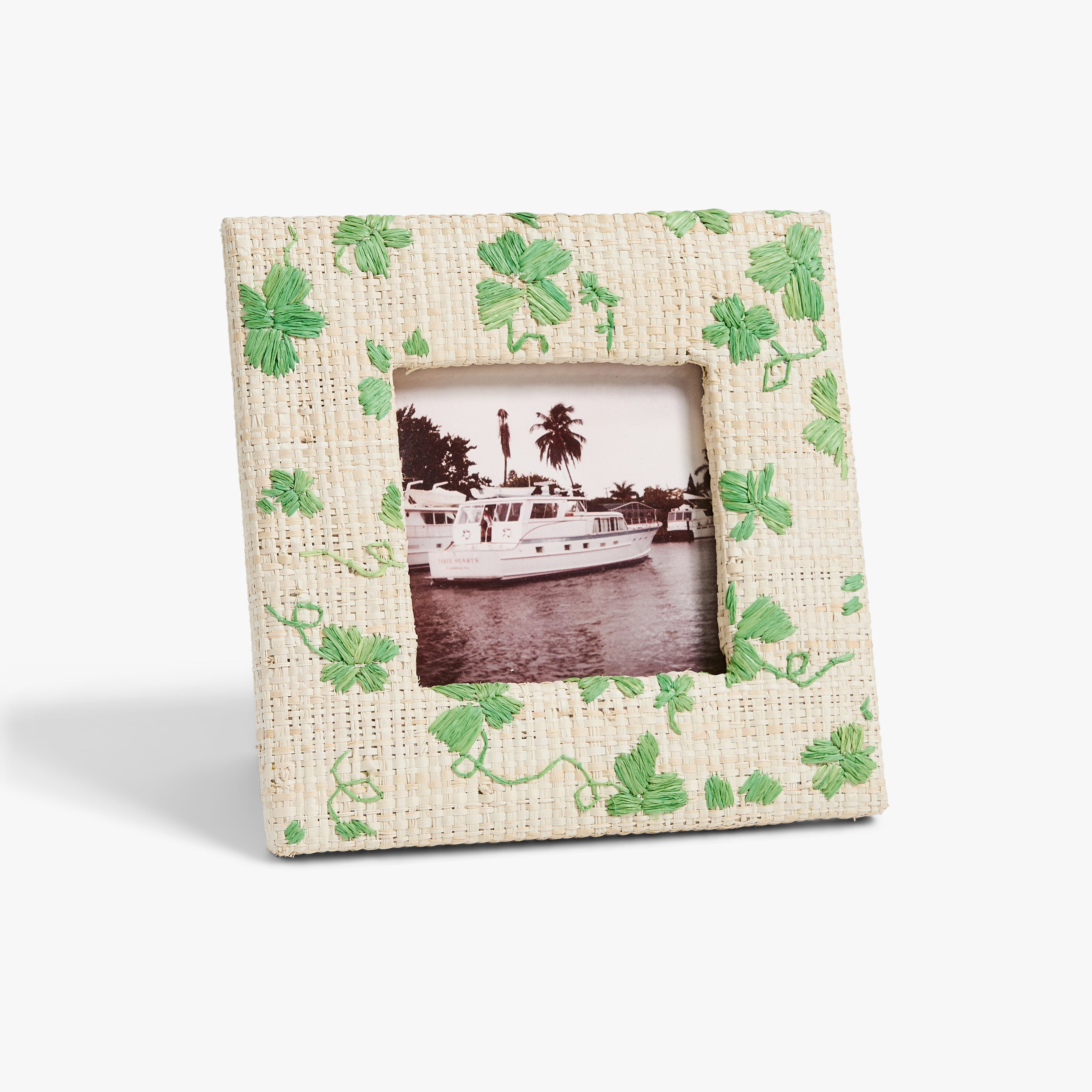 Textured frame with green clover embroidery , featuring a black-and-white image of a boat on water with palm trees in the background.