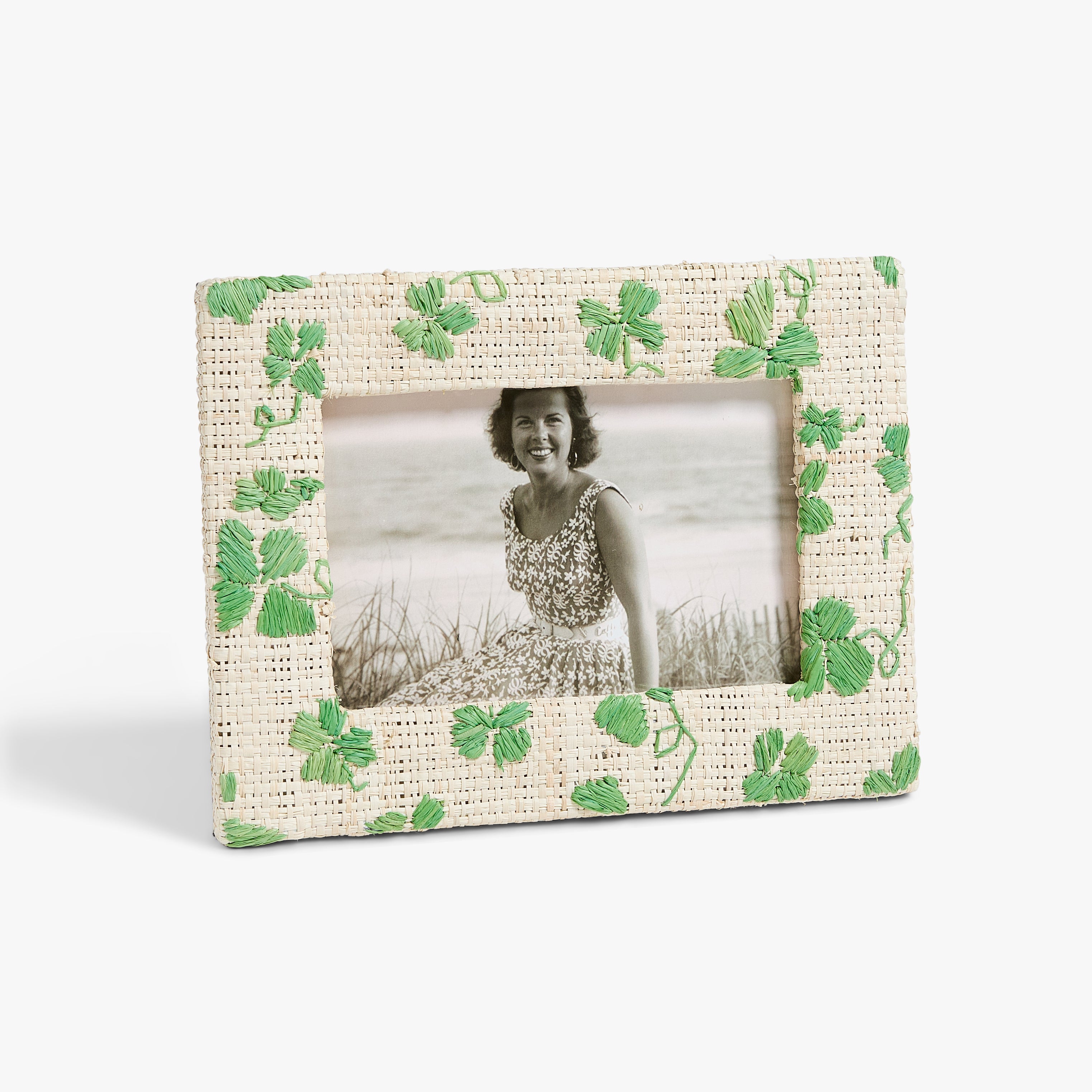Vintage photo in a textured frame with green clover embroidery. Smiling woman in a floral dress sits on a beach.