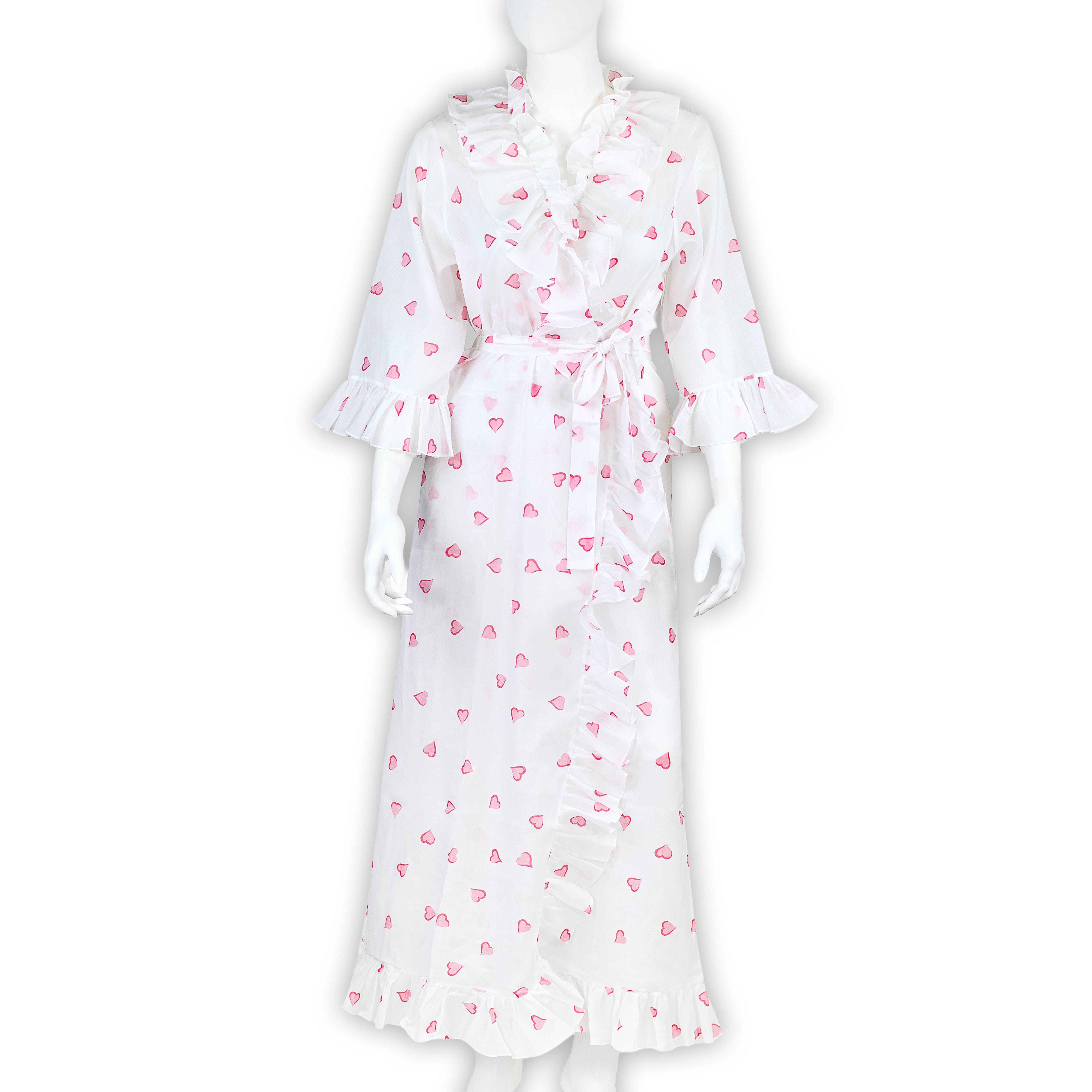 Scattered pink hearts on cotton voile bias cut long nightgown with waist tie and V-neck, ruffles in front, back and on sleeve cuffs. Displayed on mannequin with a white background.