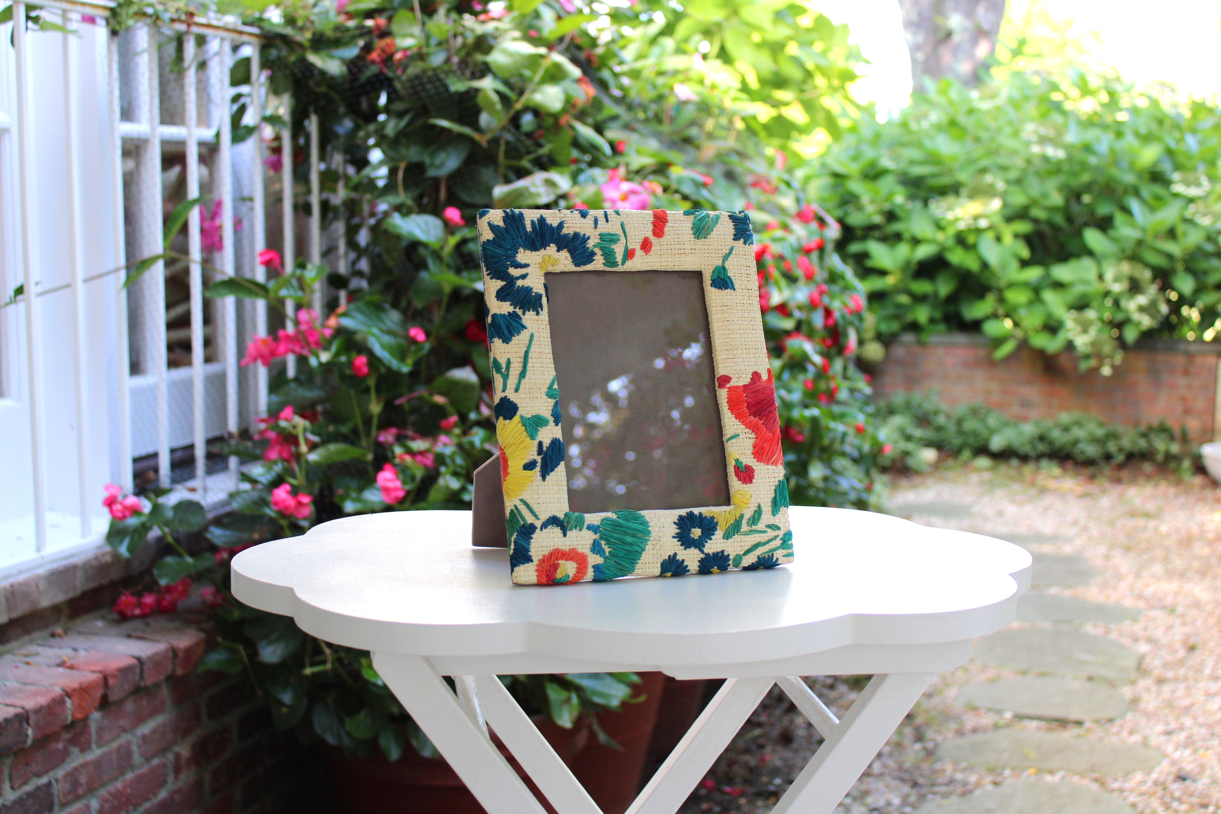 Floral photo frame on a white table outdoors with greenery and flowers in the background