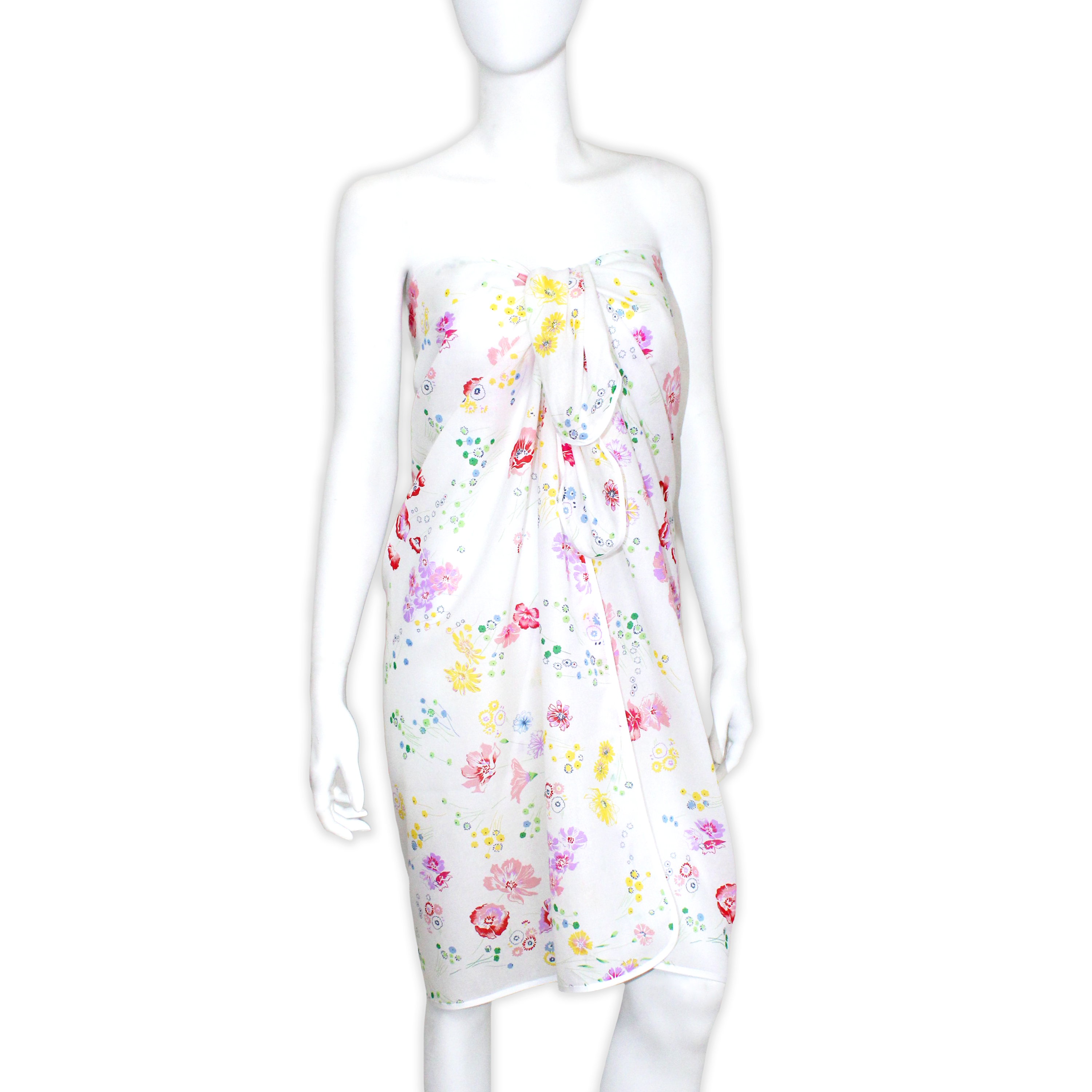 White mannequin wearing a strapless pareo in Fleurs d’Aril print, adorned with delicate multicolor florals in pink, yellow, blue, and green on a white background. Pareo is tied at the front and falling to knee length. Finished with a White bias.