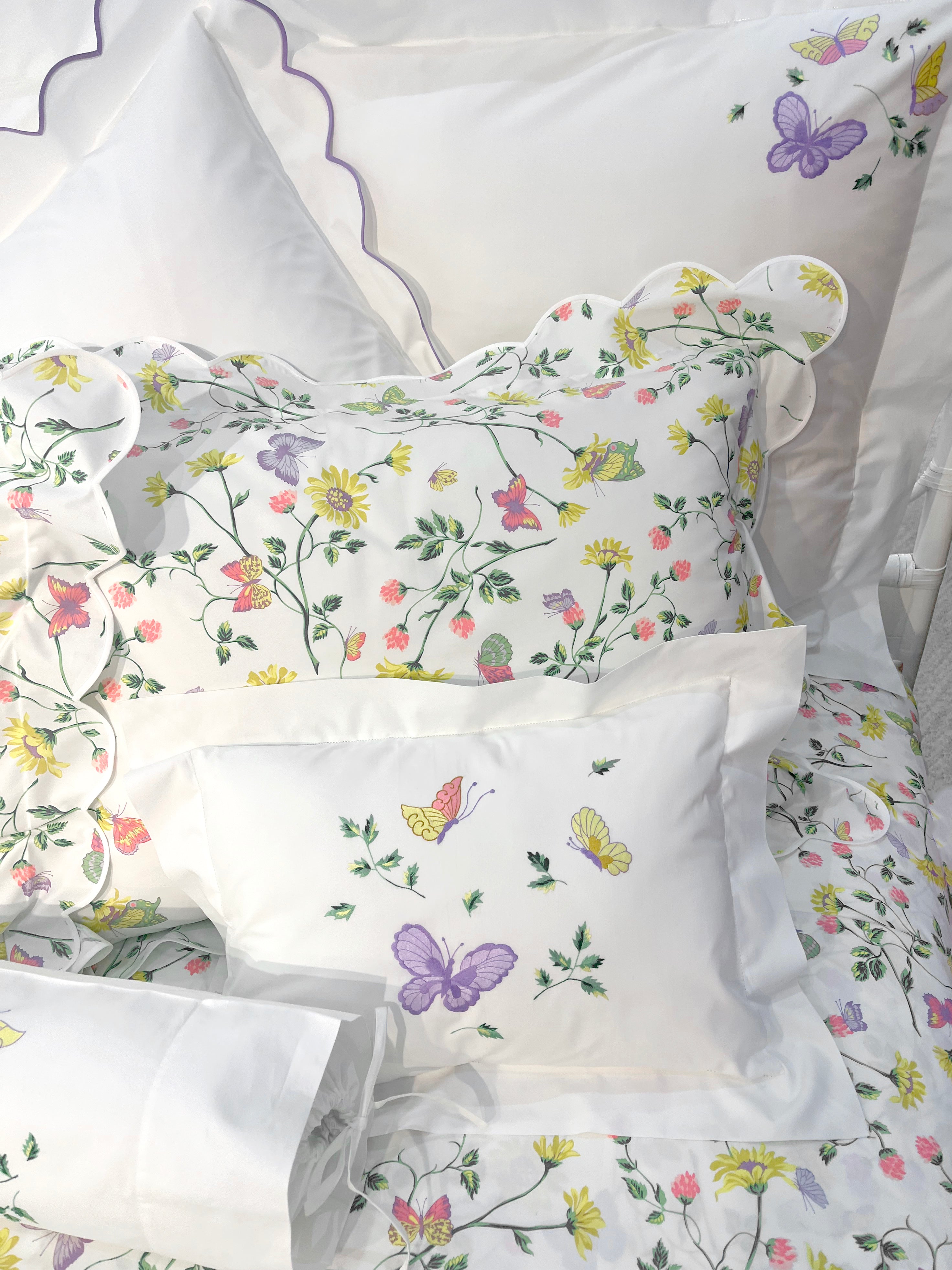 Printed and embroidered florals and butterflies (in pink, yellow, lilac and green) bed linens displayed on bed.
