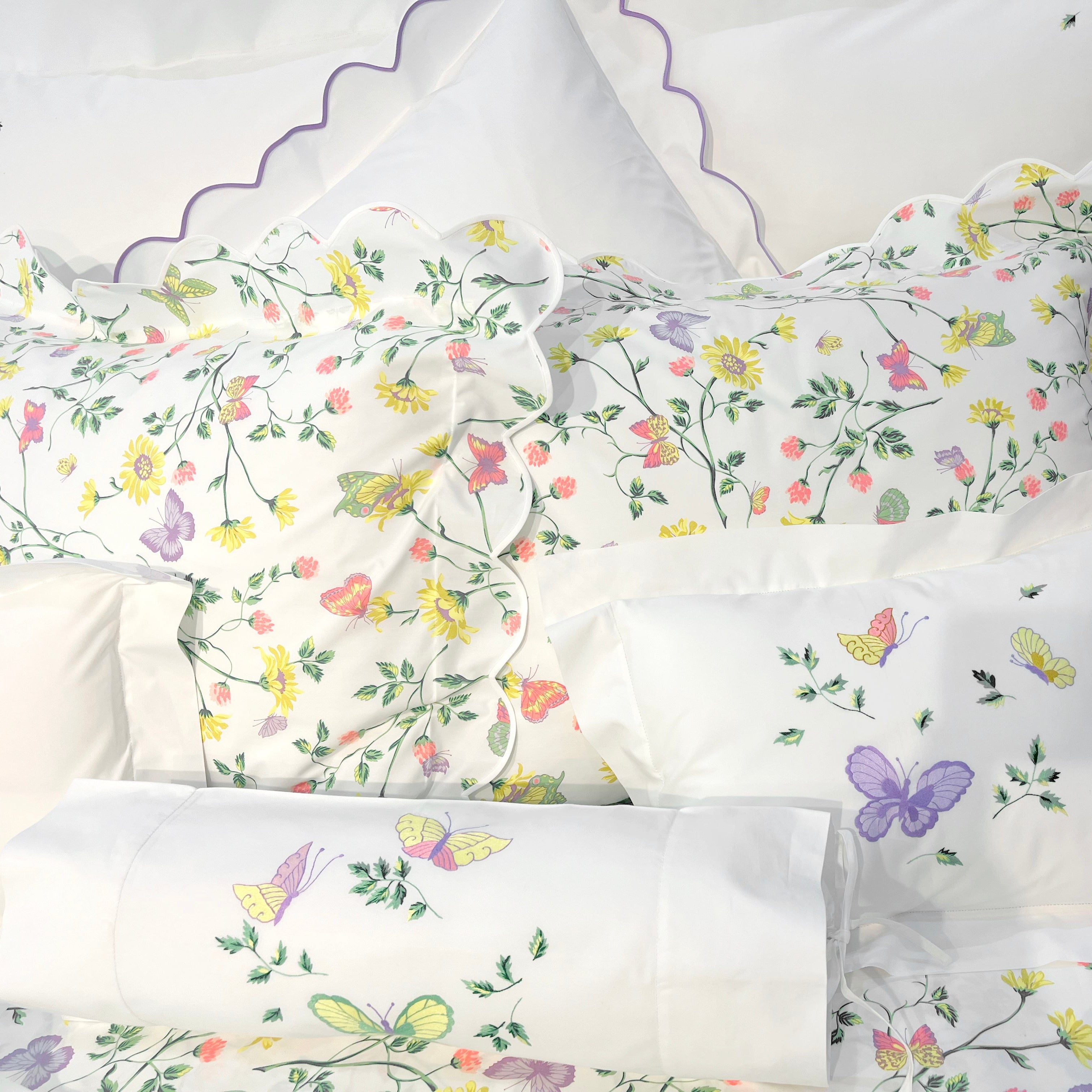 Printed and embroidered florals and butterflies (in pink, yellow, lilac and green) bed linens displayed on bed.