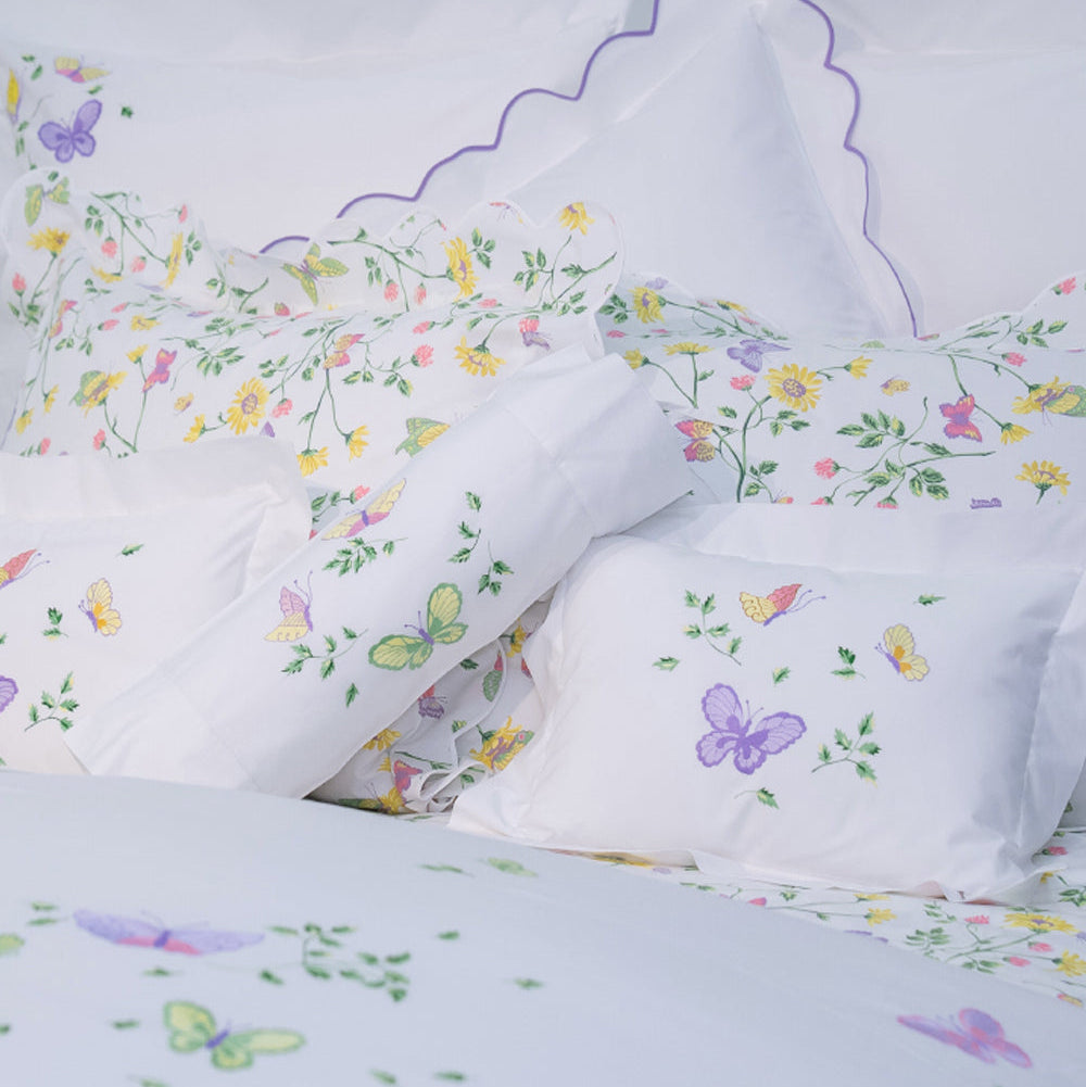 Printed and embroidered florals and butterflies (in pink, yellow, lilac and green) bed linens displayed on bed.