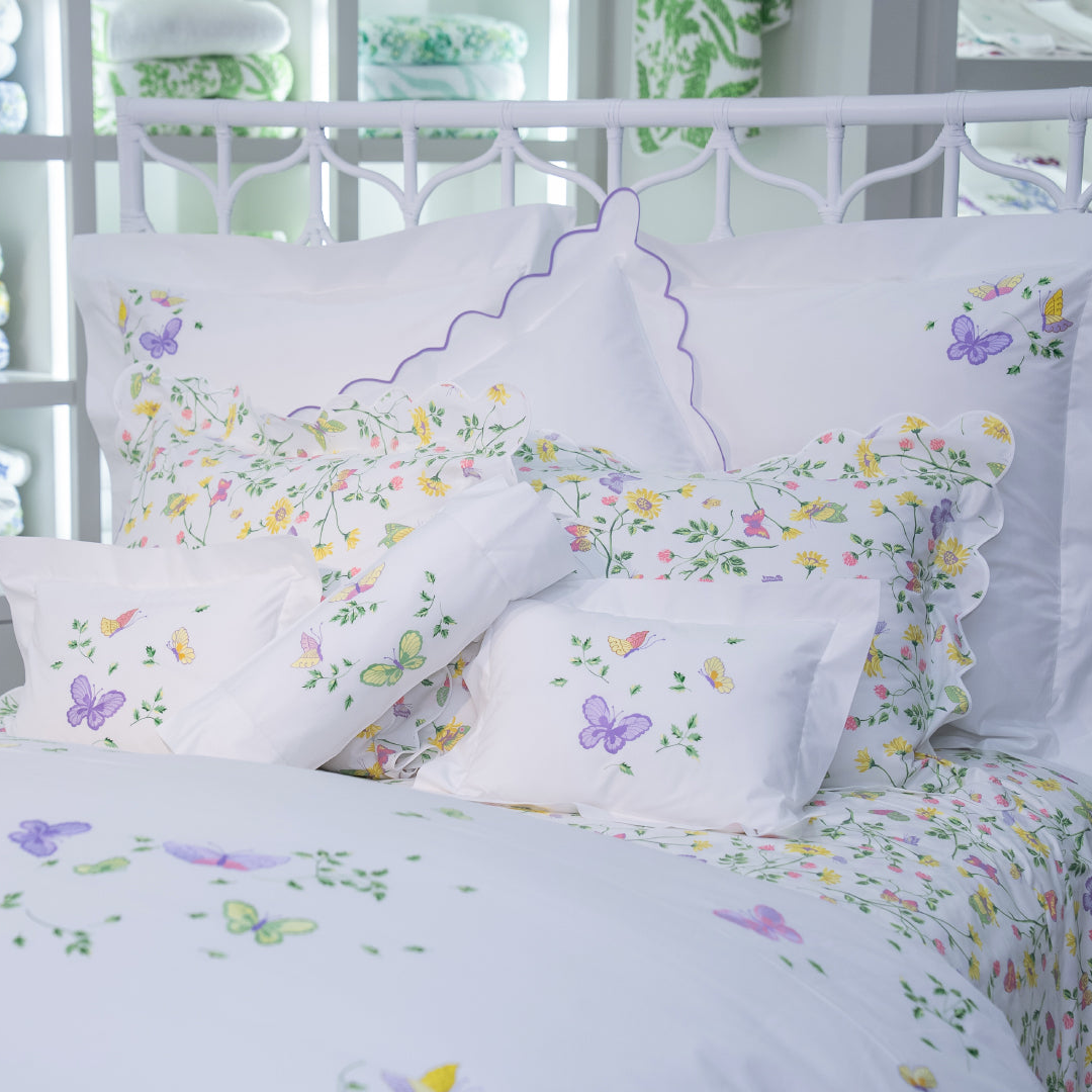 Printed and embroidered florals and butterflies (in pink, yellow, lilac and green) bed linens displayed on bed.