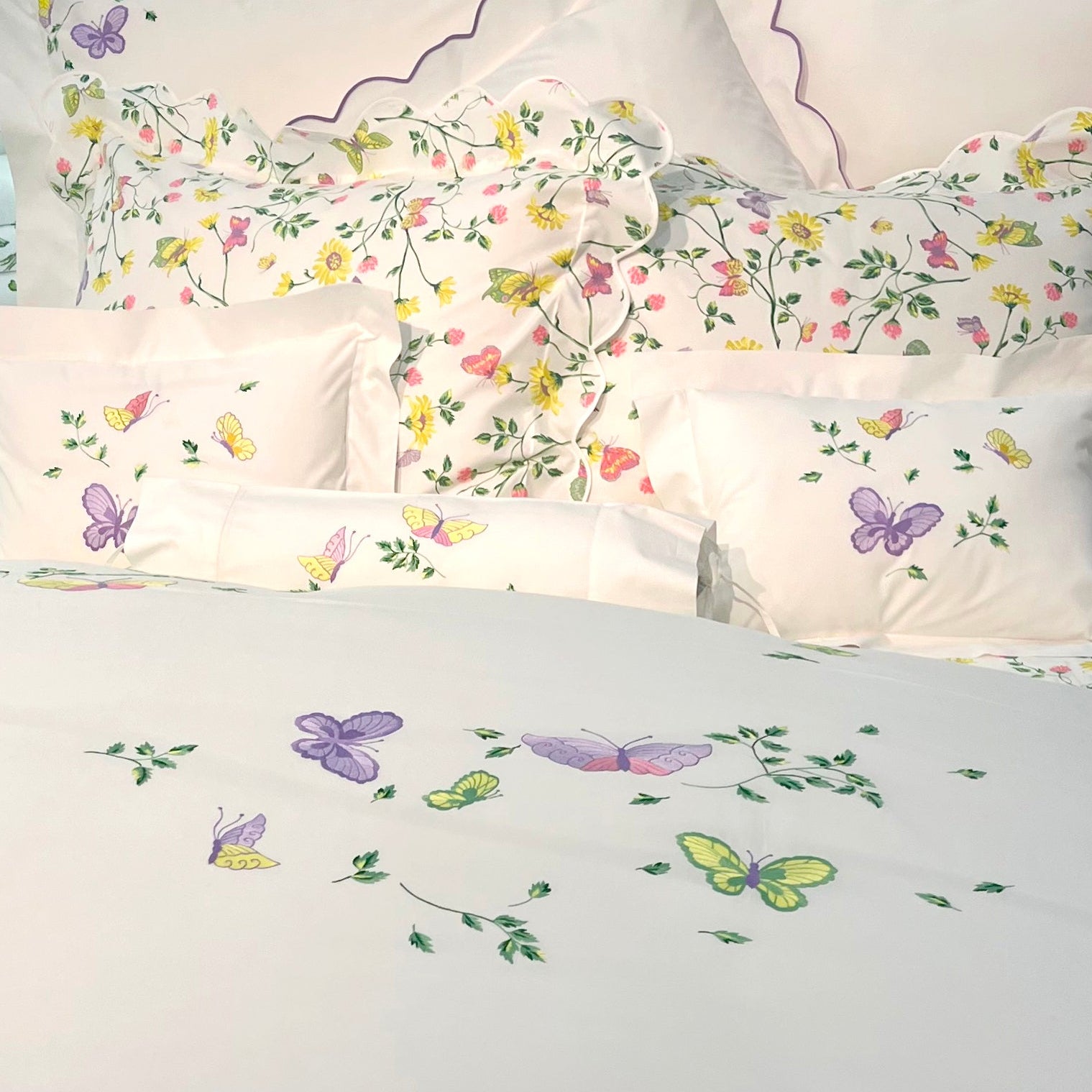 Printed and embroidered florals and butterflies (in pink, yellow, lilac and green) bed linens displayed on bed.