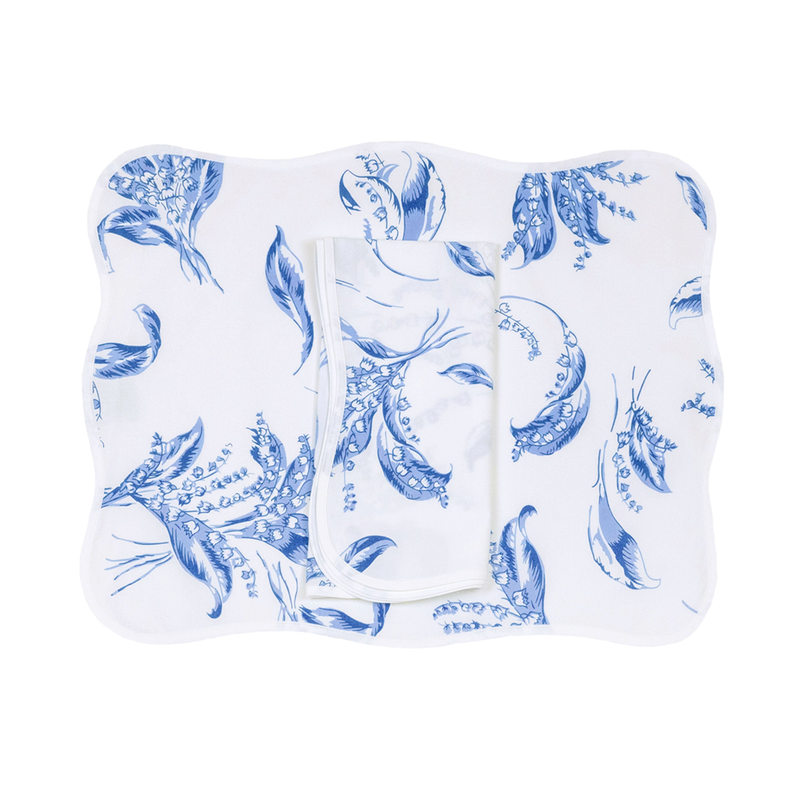 Blue lily of the valley florals, Muguet print, shown on placemat with a folded napkin, finished with a wavy white bias, on a white background.