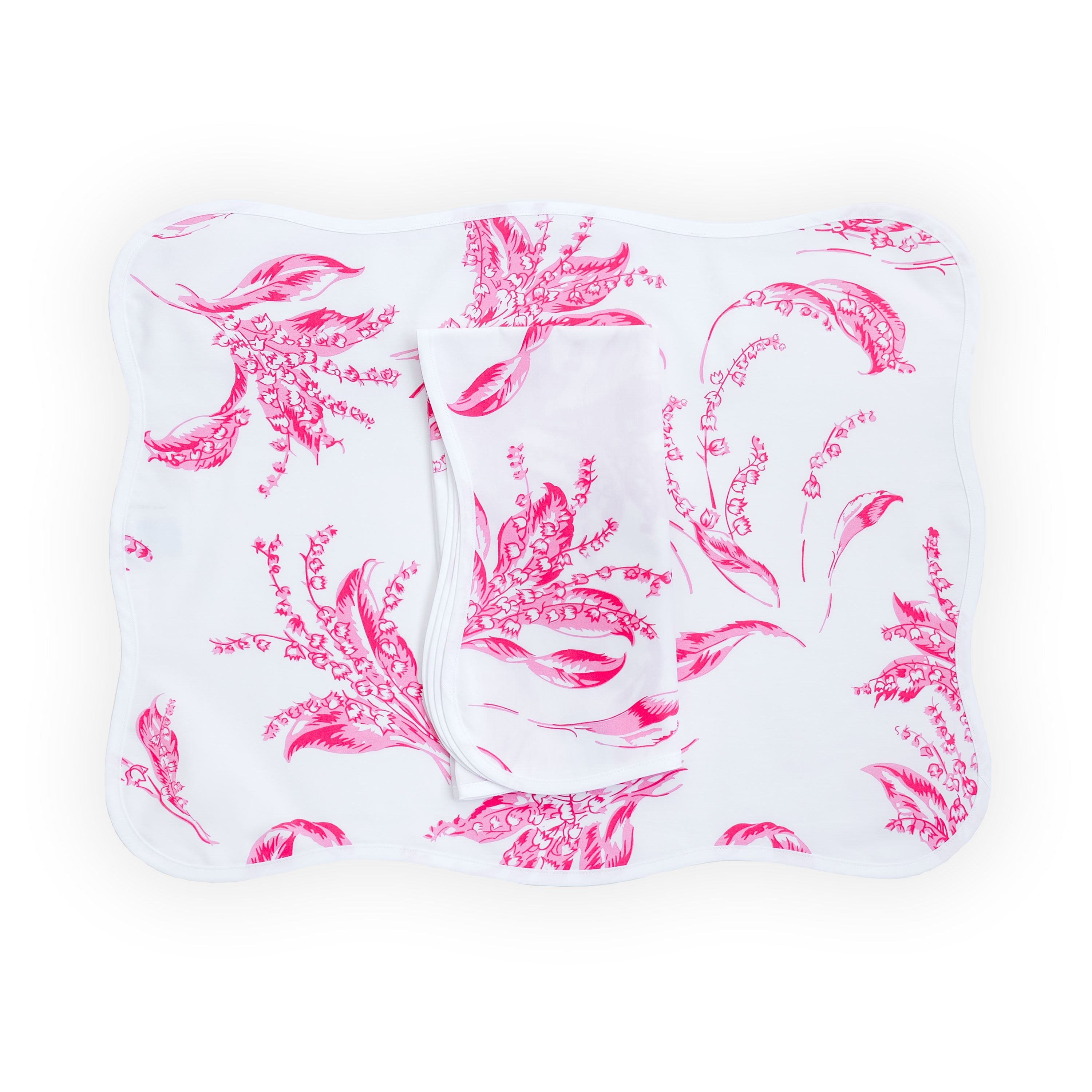 Pink lily of the valley florals, Muguet print, shown on placemat with a folded napkin, finished with a wavy white bias, on a white background.