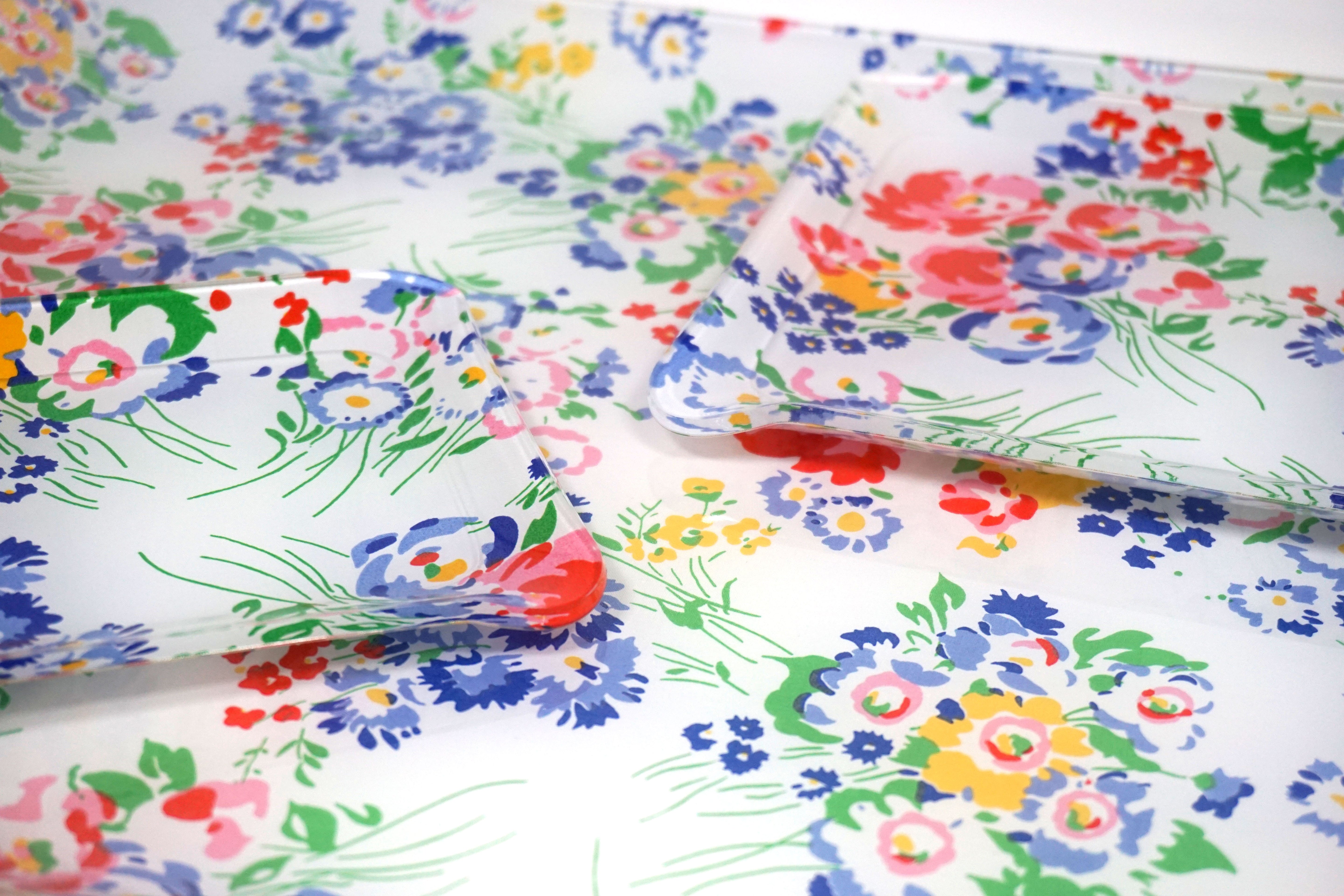 Printed Laminated Trays, side view of small and medium size trays on top of large tray. Each tray in multi color blue, pink, yellow and red floral with green leaves/stems, New York Mille Fleurs print.