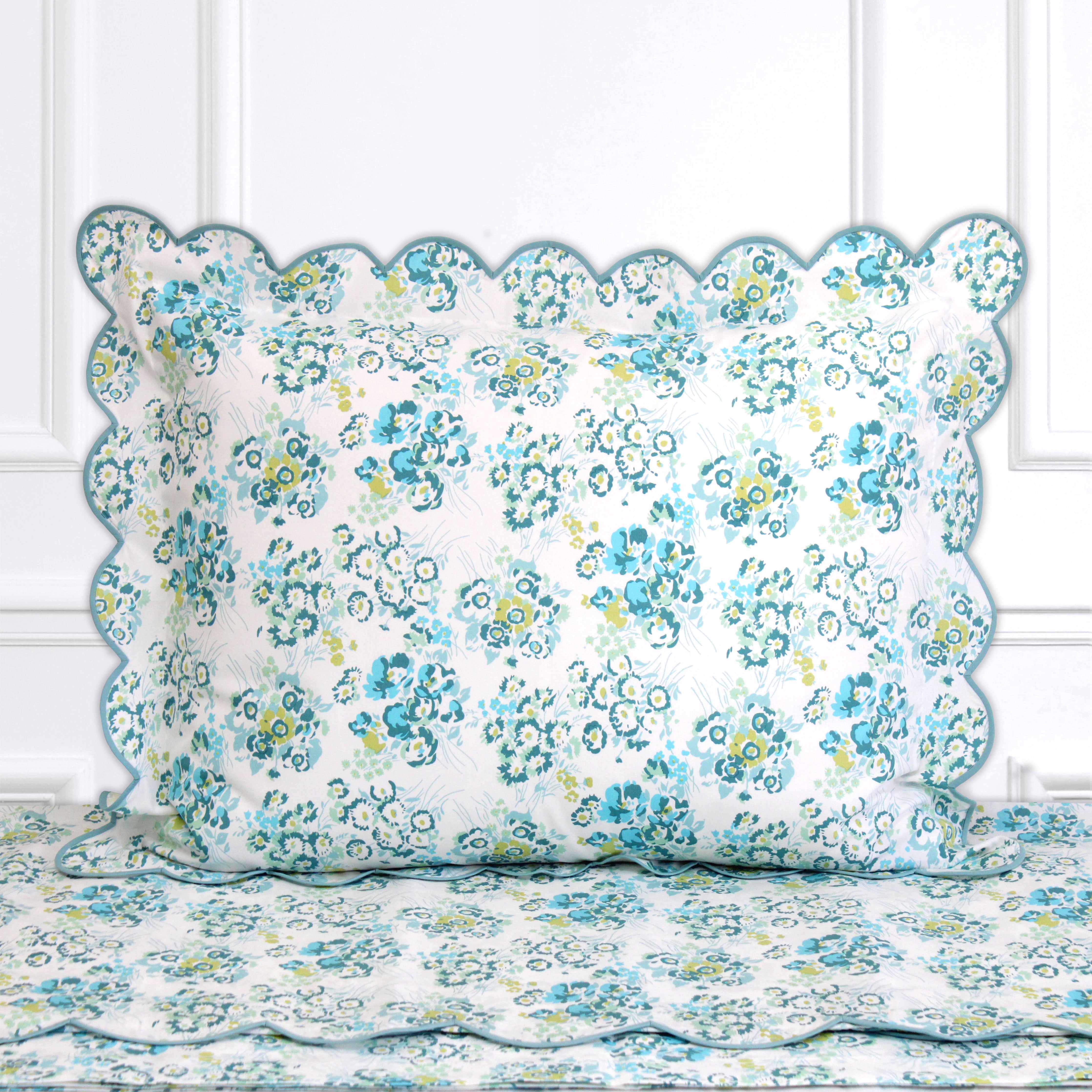 Blue and green florals, New York Mille Fleurs print shown on a Standard Sham with a scallop dp blue bias, on top of matching bed sheet with a white panel background.