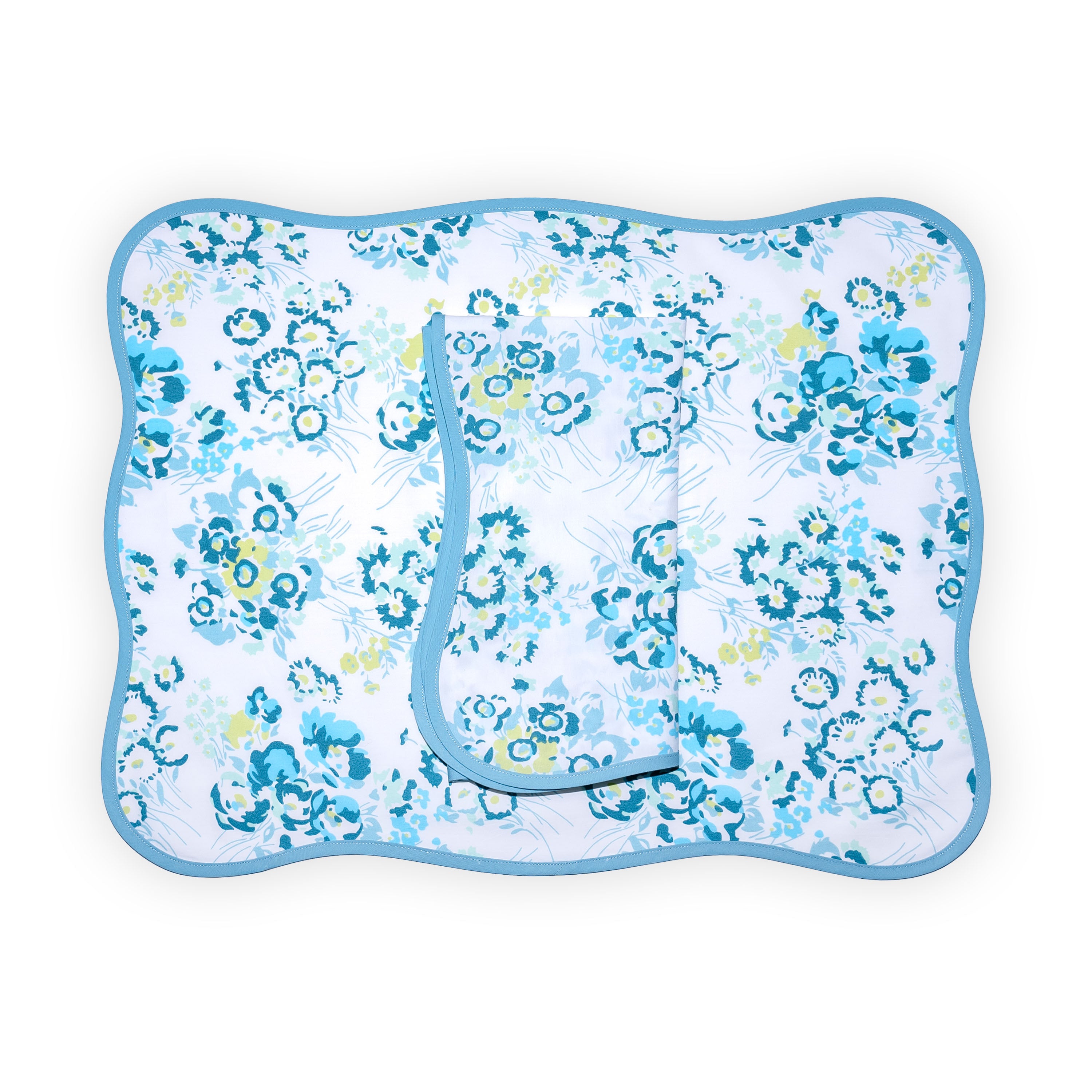 Blue florals, New York Mille Fleurs print, shown on placemat with a folded napkin, finished with a wavy blue bias, on a white background.
