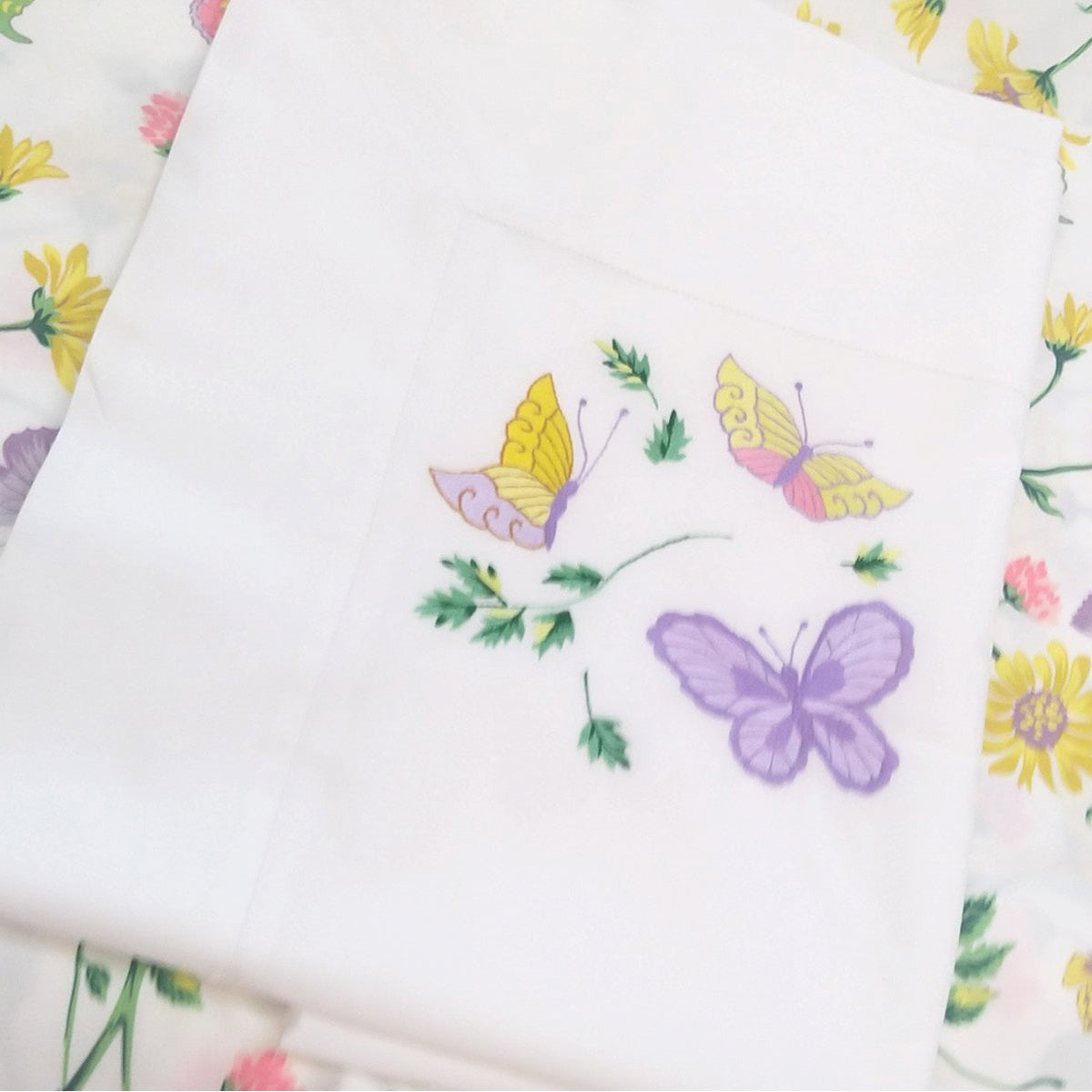 Printed and embroidered florals and butterflies (in pink, yellow, lilac and green) sham displayed on bed.