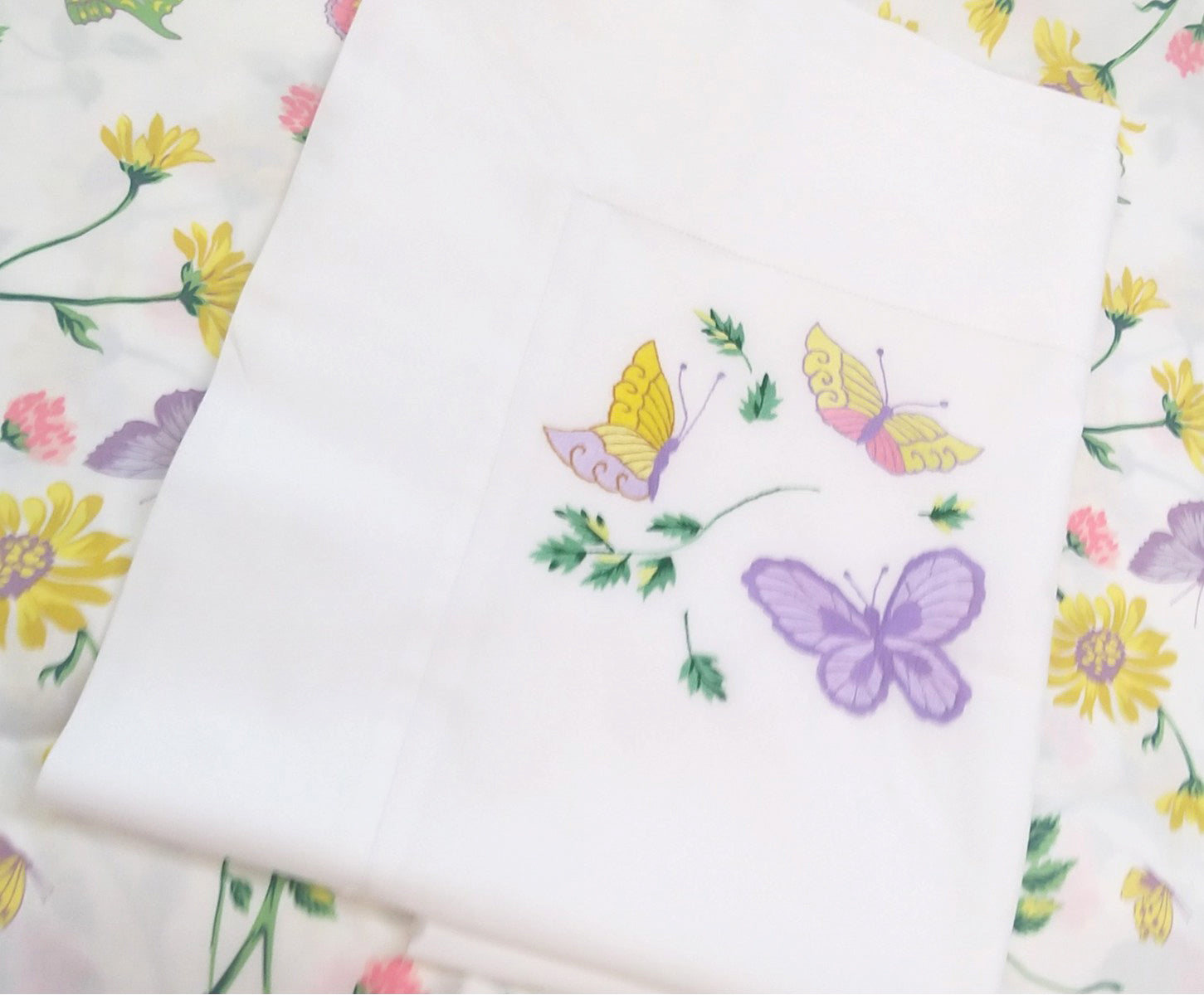 Printed and embroidered florals and butterflies (in pink, yellow, lilac and green) sham displayed on bed.