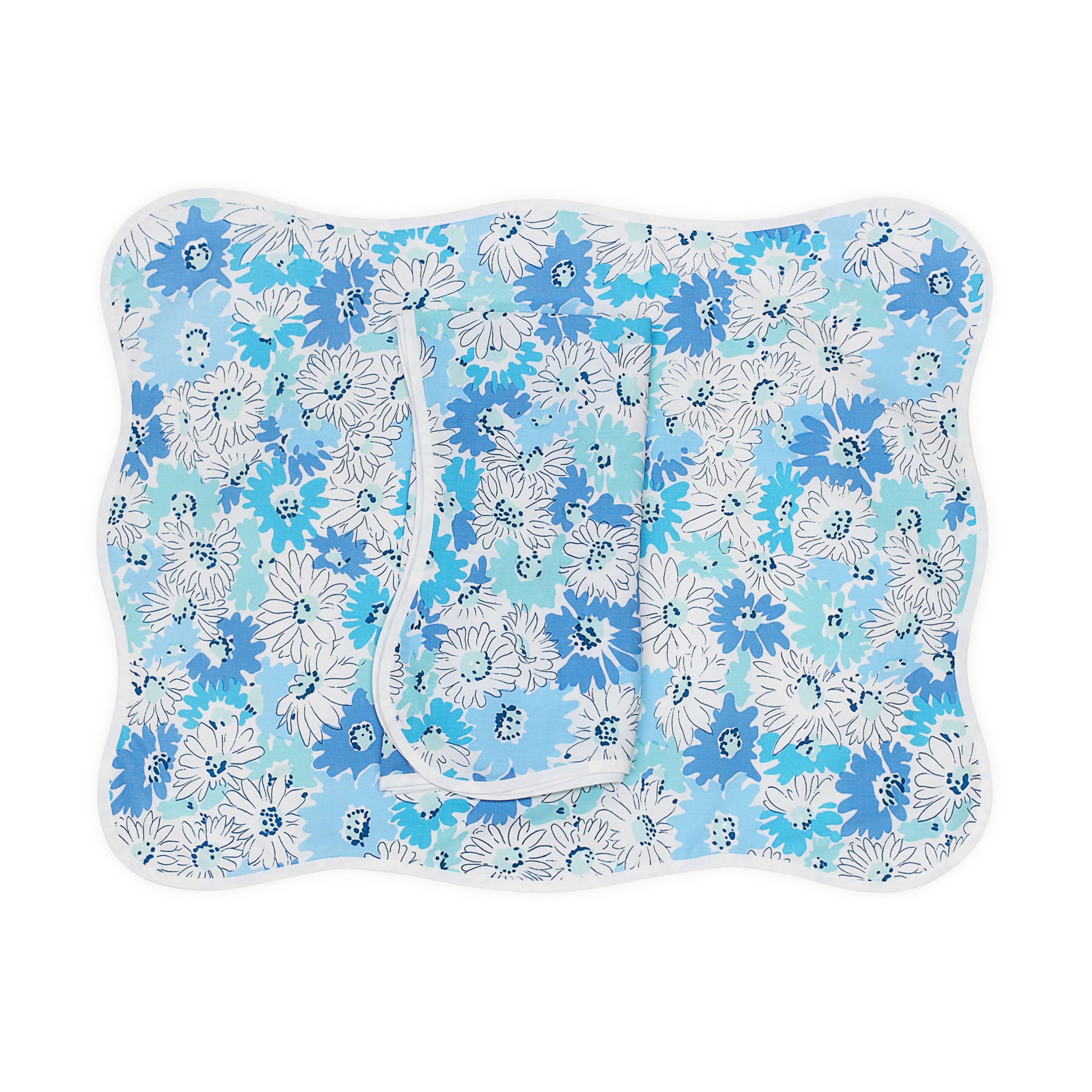 Blue florals, Petite Marguerite print, shown on placemat with a folded napkin, finished with a wavy white bias, on a white background.