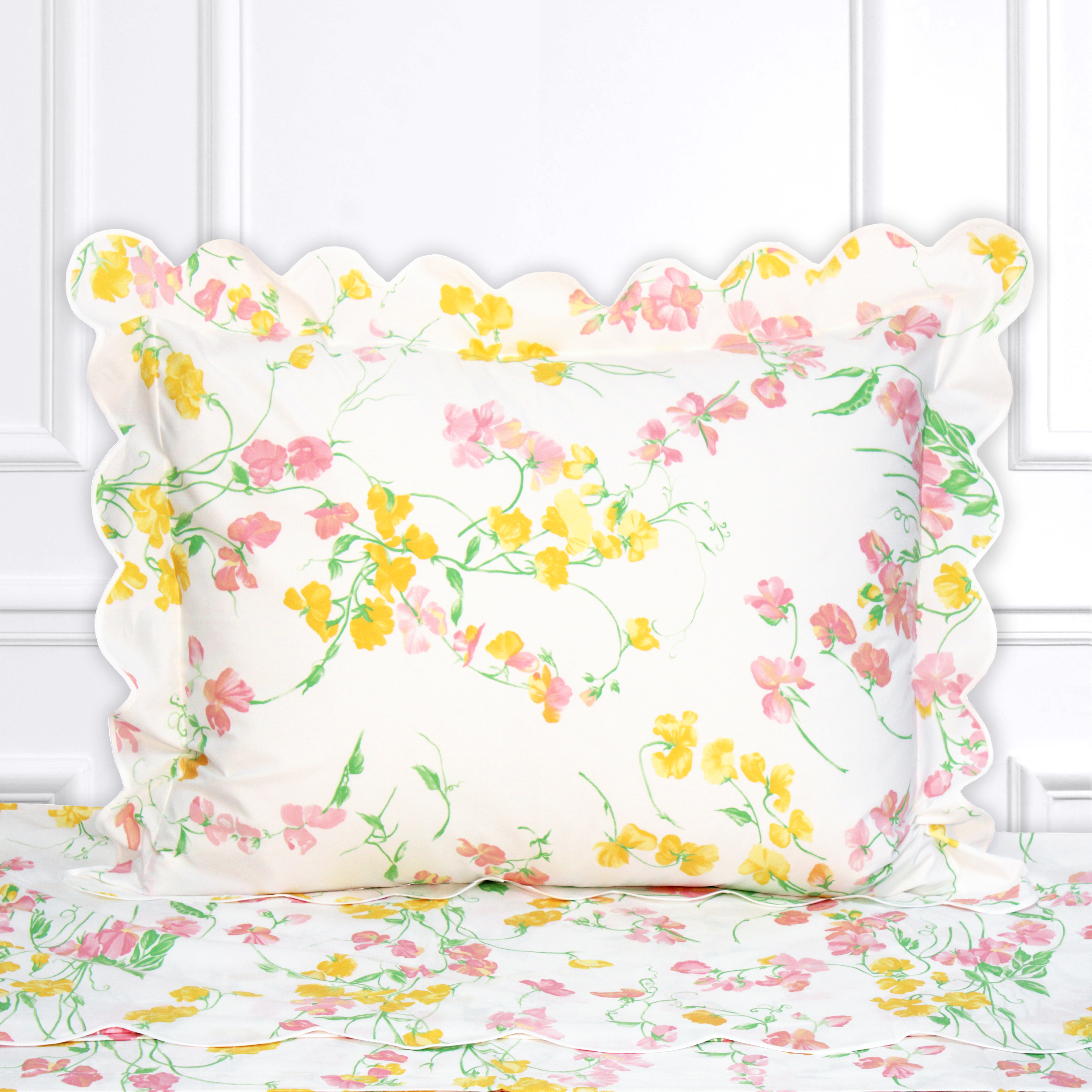 Pink and yellow florals (sweet peas) with green leaves/stems, Pois de Senteur print, shown on a Standard Sham with a scallop blue bias, on top of matching bed sheet with a white panel background.