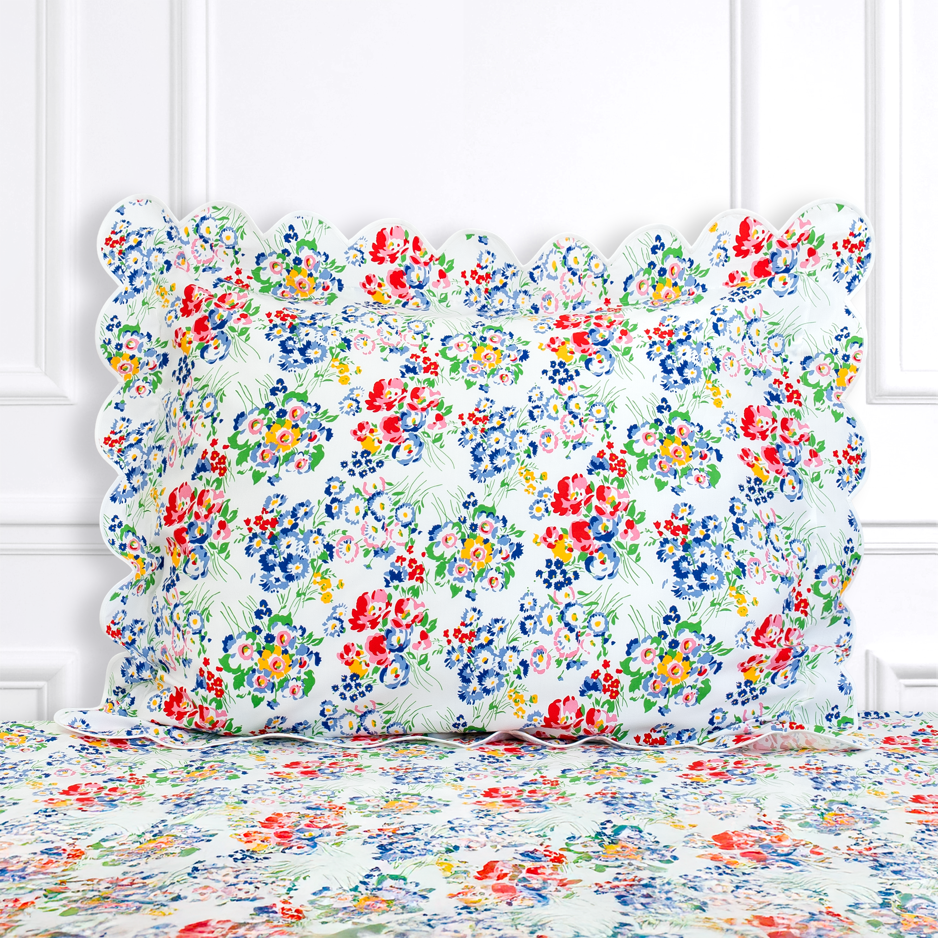 Multi color floral, New York Mille Fleurs print shown on a Standard Sham with a scallop white bias, on top of matching bed sheet with a white panel background.