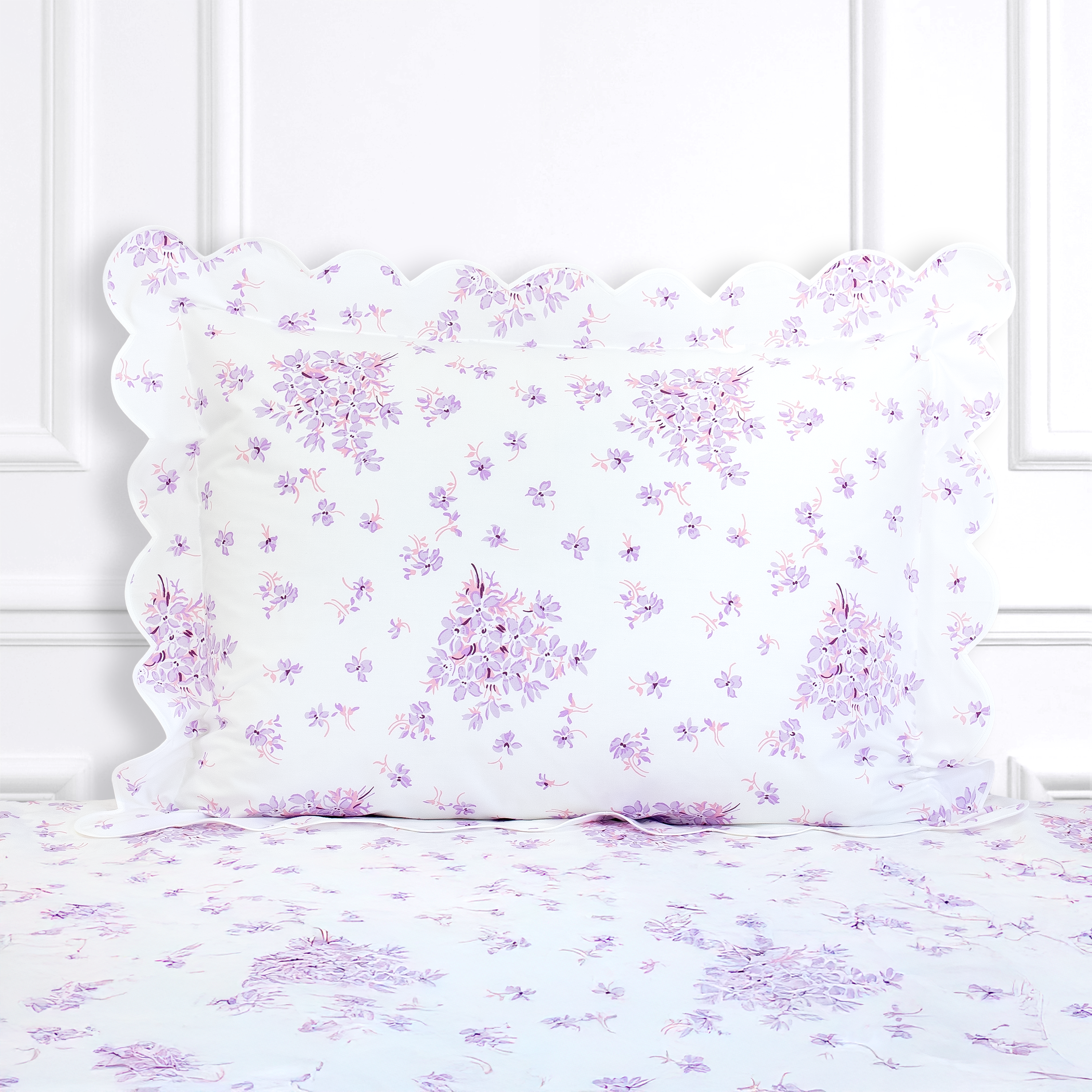 Lilac floral with pink center and dark purple leaves, Violettes print shown on a Standard Sham with a scallop white bias, on top of matching bed sheet with a white panel background.