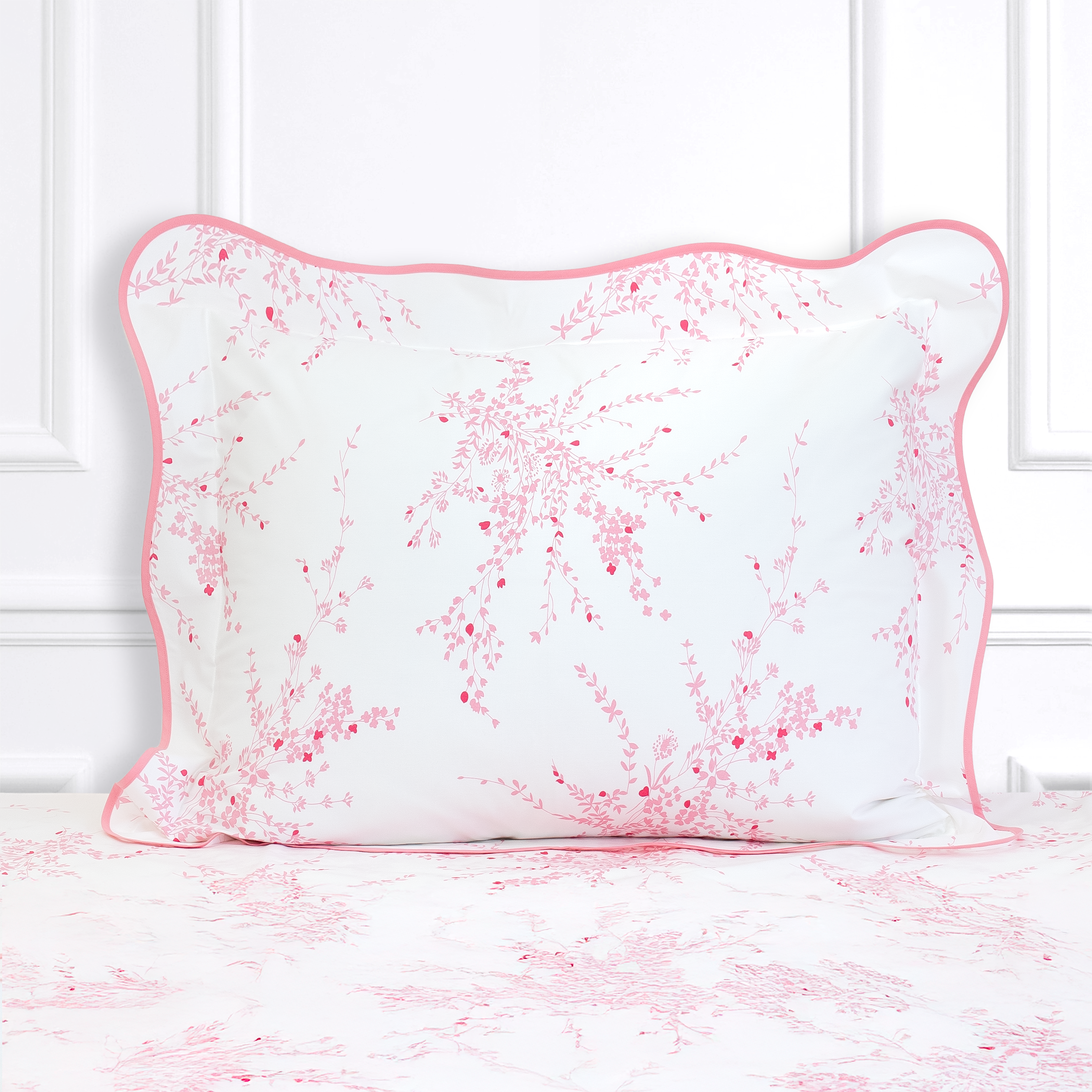 Pink florals, Jete de Fleurs print shown on a Standard Sham with a wavy pink bias, on top of matching bed sheet with a white panel background.