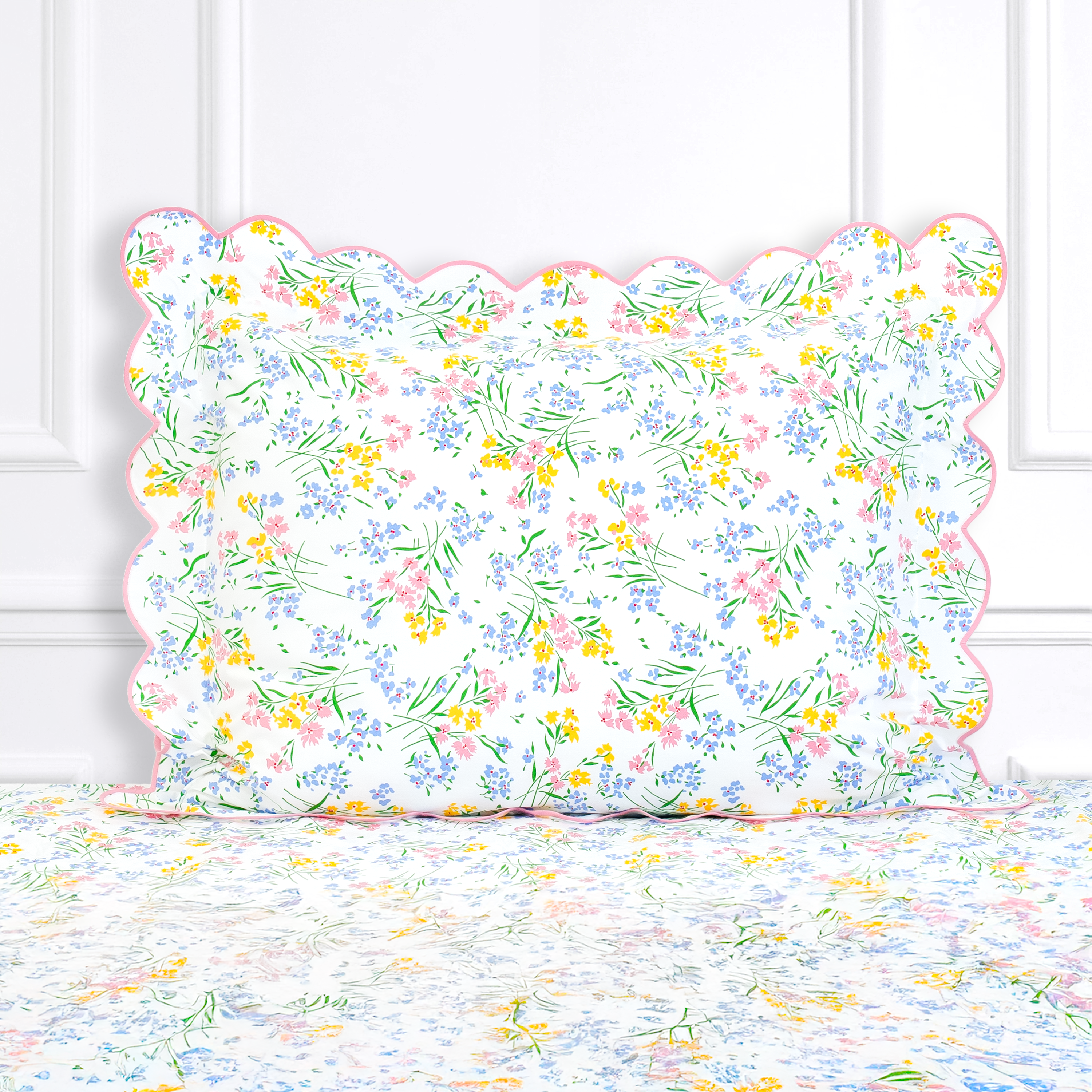Multi color florals with green leaves and stems, Fleurs des Champs print shown on a Standard Sham with a scallop pink bias, on top of matching bed sheet with a white panel background.