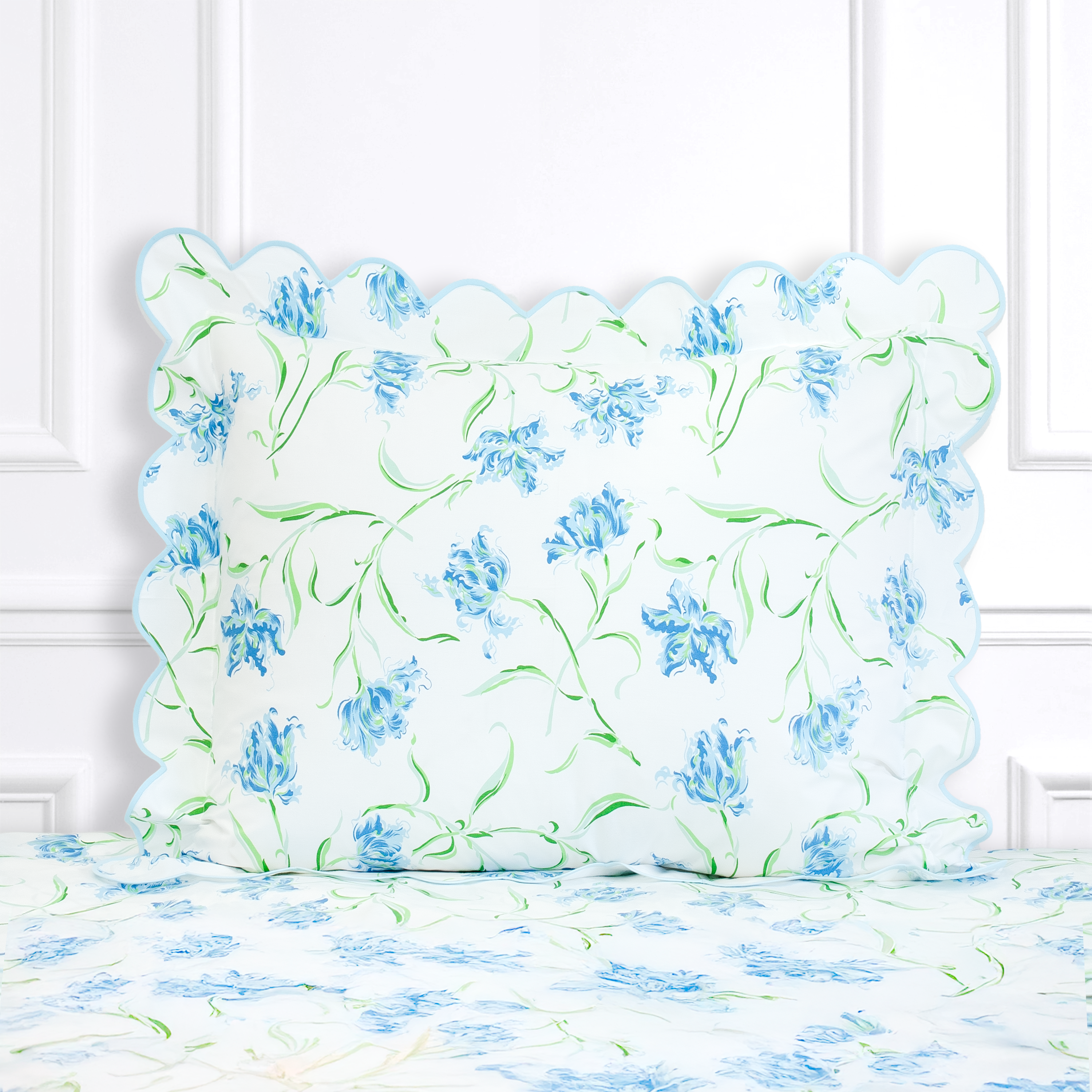 Blue floral with green leaves and stems, Tulipe Perroquet print shown on a Standard Sham with a scallop blue bias, on top of matching bed sheet with a white panel background.