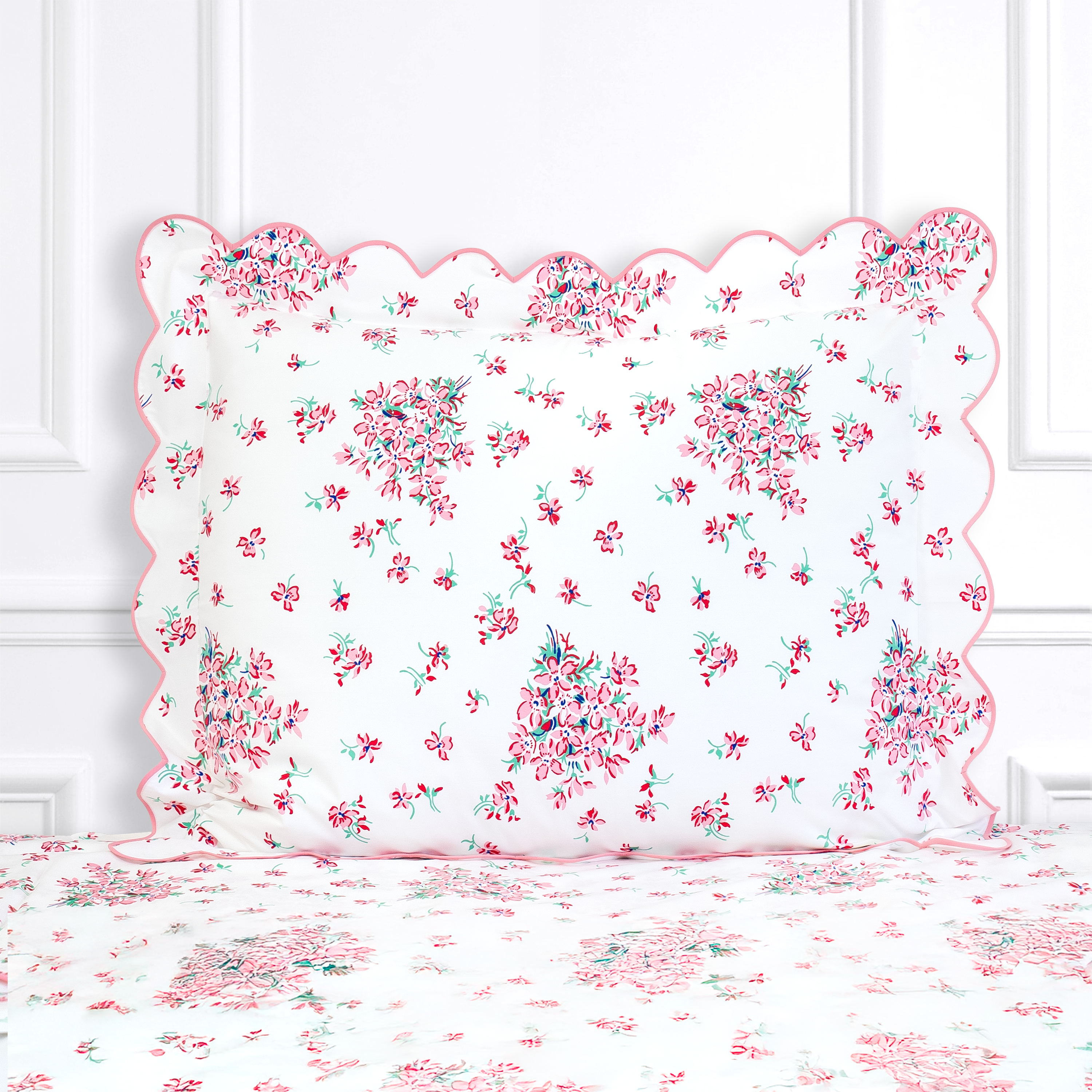 Pink floral with red center and green leaves, Violettes print shown on a Standard Sham with a scallop pink bias, on top of matching bed sheet with a white panel background.