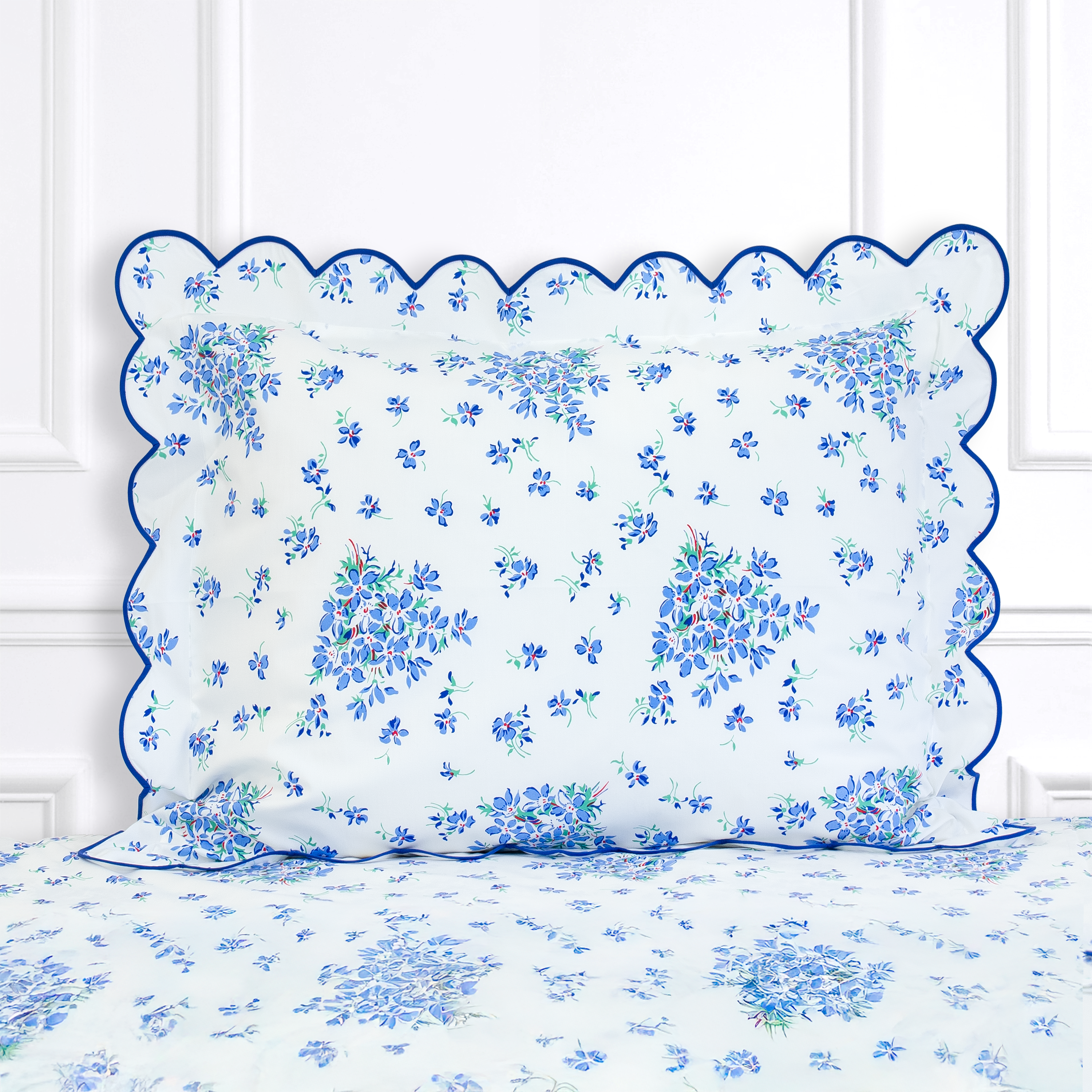 Blue color floral with red center and green leaves, Violettes print shown on a Standard Sham with a scallop blue bias, on top of matching bed sheet with a white panel background.