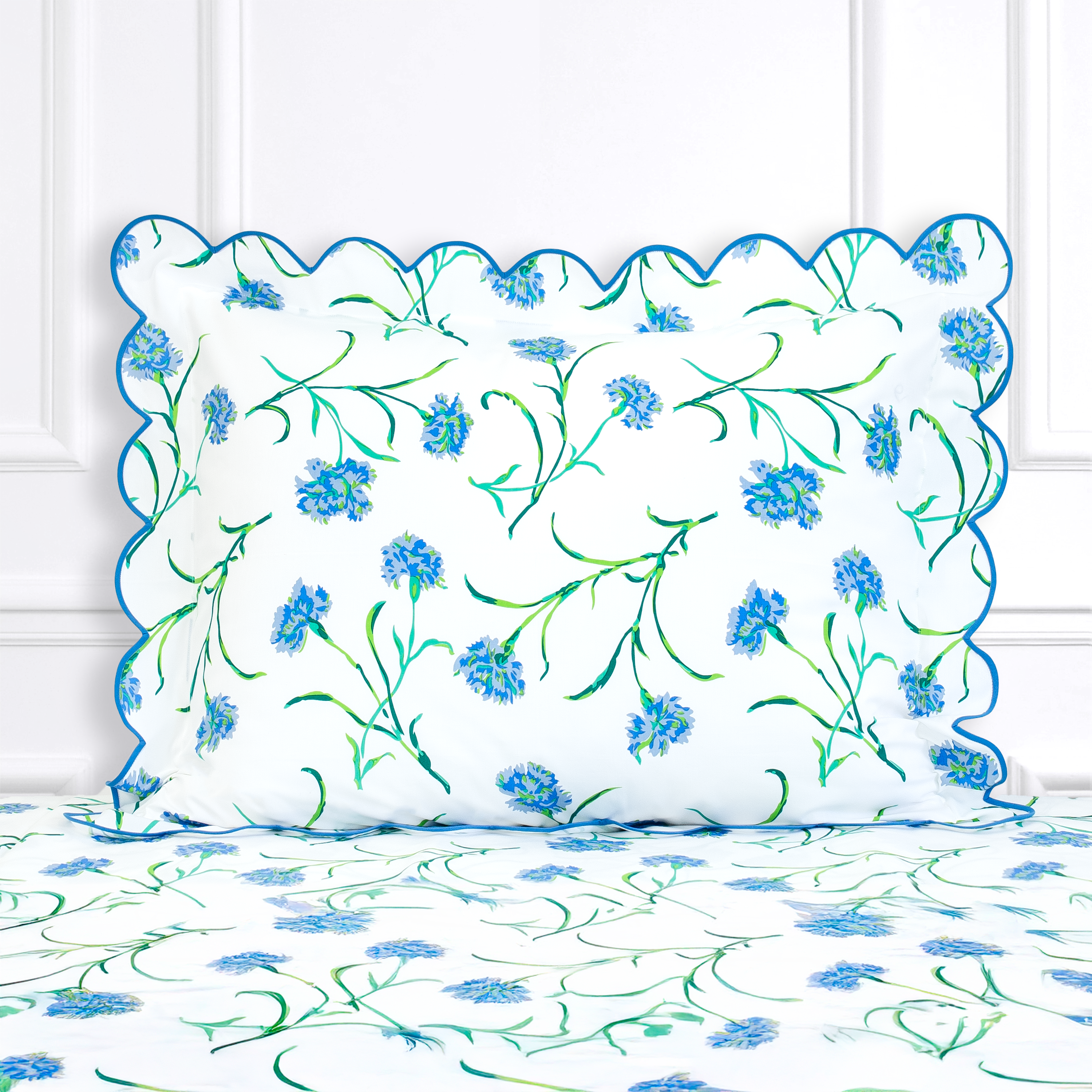 Blue and green color floral, Carnations print shown on a Standard Sham with a scallop blue bias, on top of matching bed sheet with a white panel background.