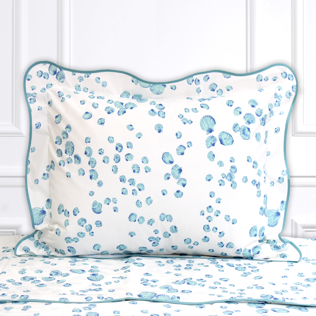 Blue seashells, Shells print, shown on a Standard Sham with a wavy blue bias, on top of matching bed sheet with a white panel background.