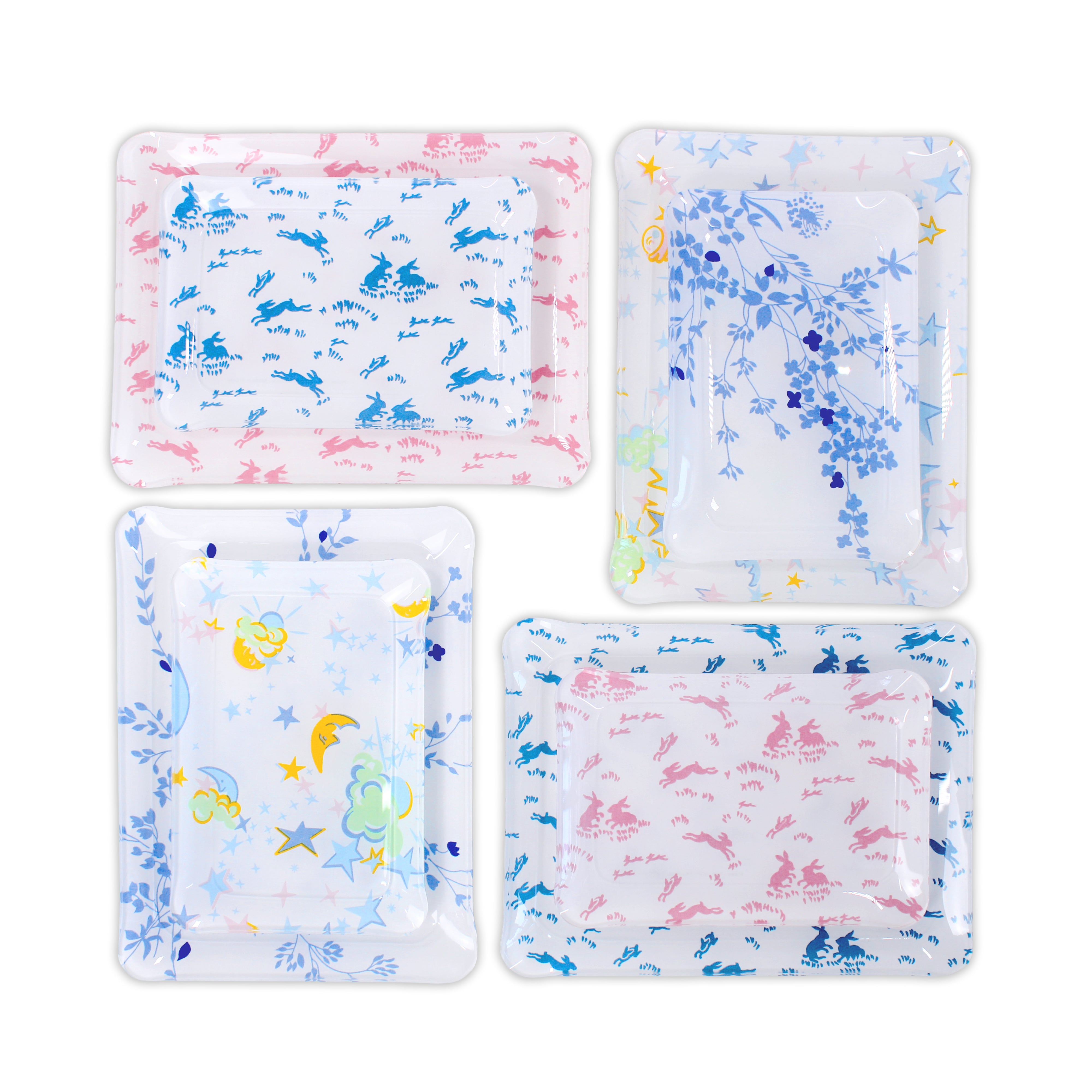 Printed Laminated Trays, group shot of 2 trays in 4 different prints; top to bottom: small and medium. Each tray in pink bunnies, blue bunnies, blue florals (Jeté de Fleurs blue print), and multicolored Moons and Stars.