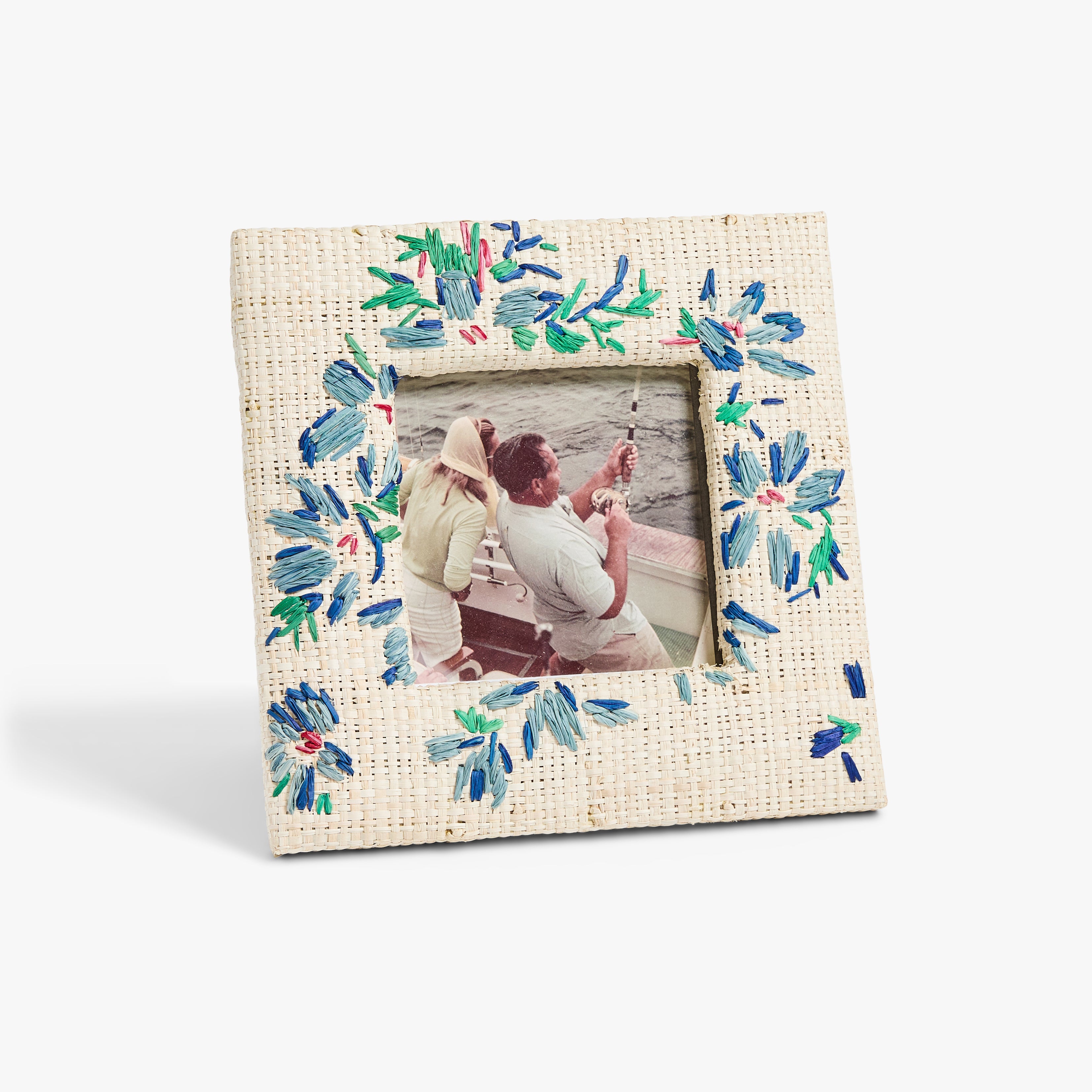 A decorated photo frame with blue and green floral patterns displays a photo of two people fishing on a boat. 